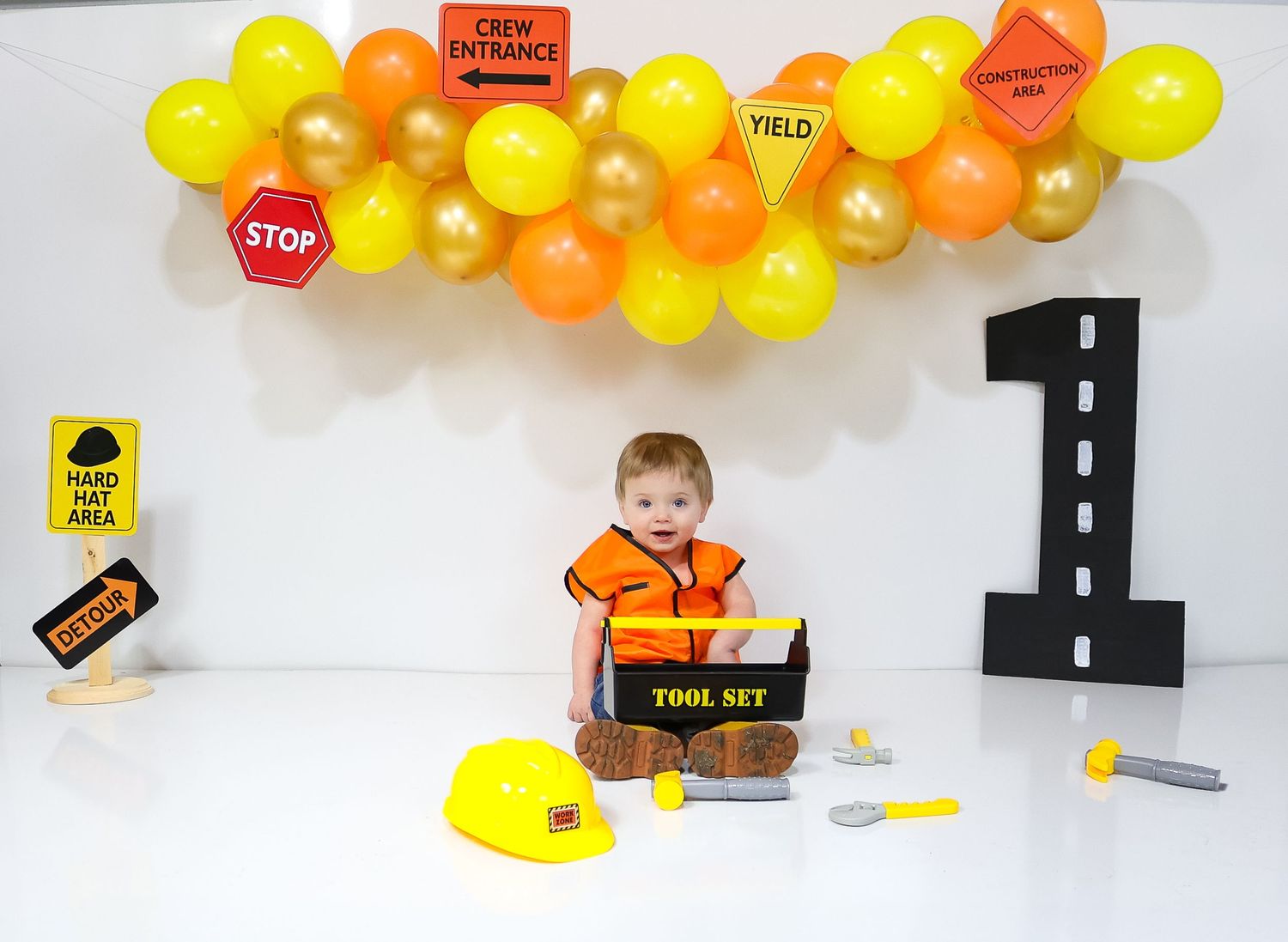 Construction themed photoshoot setup with yellow and orange balloons and traffic signs.