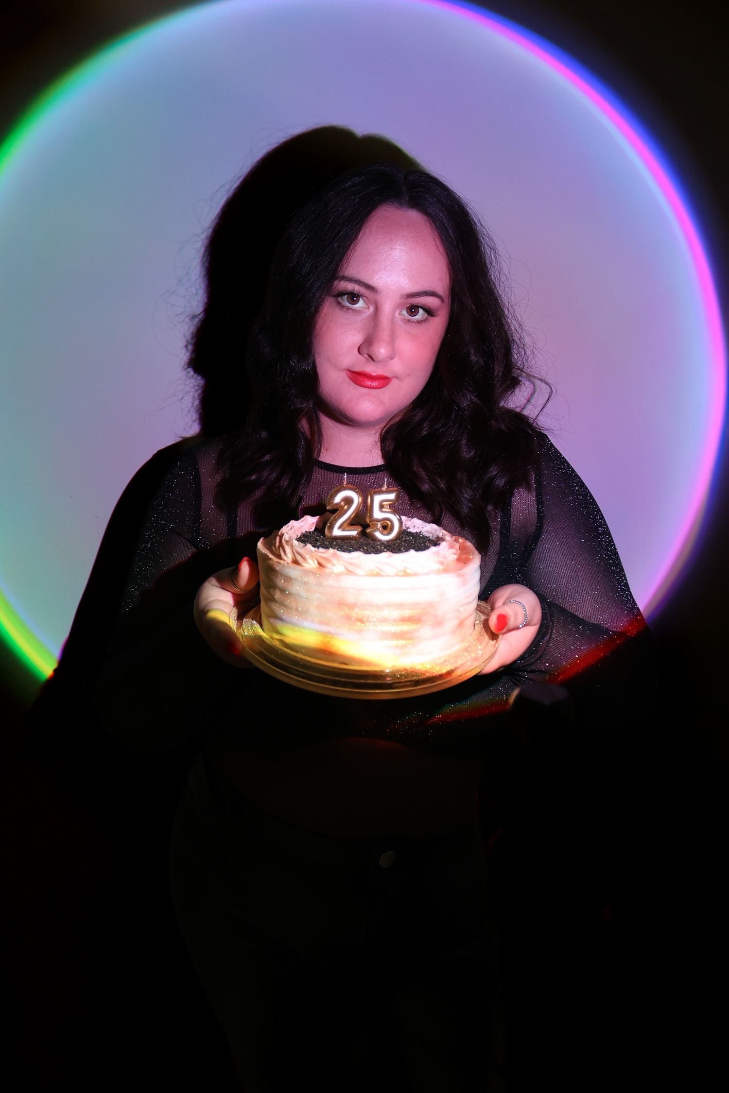 Birthday cake with glowing candles in dark room with neon lighting effects.