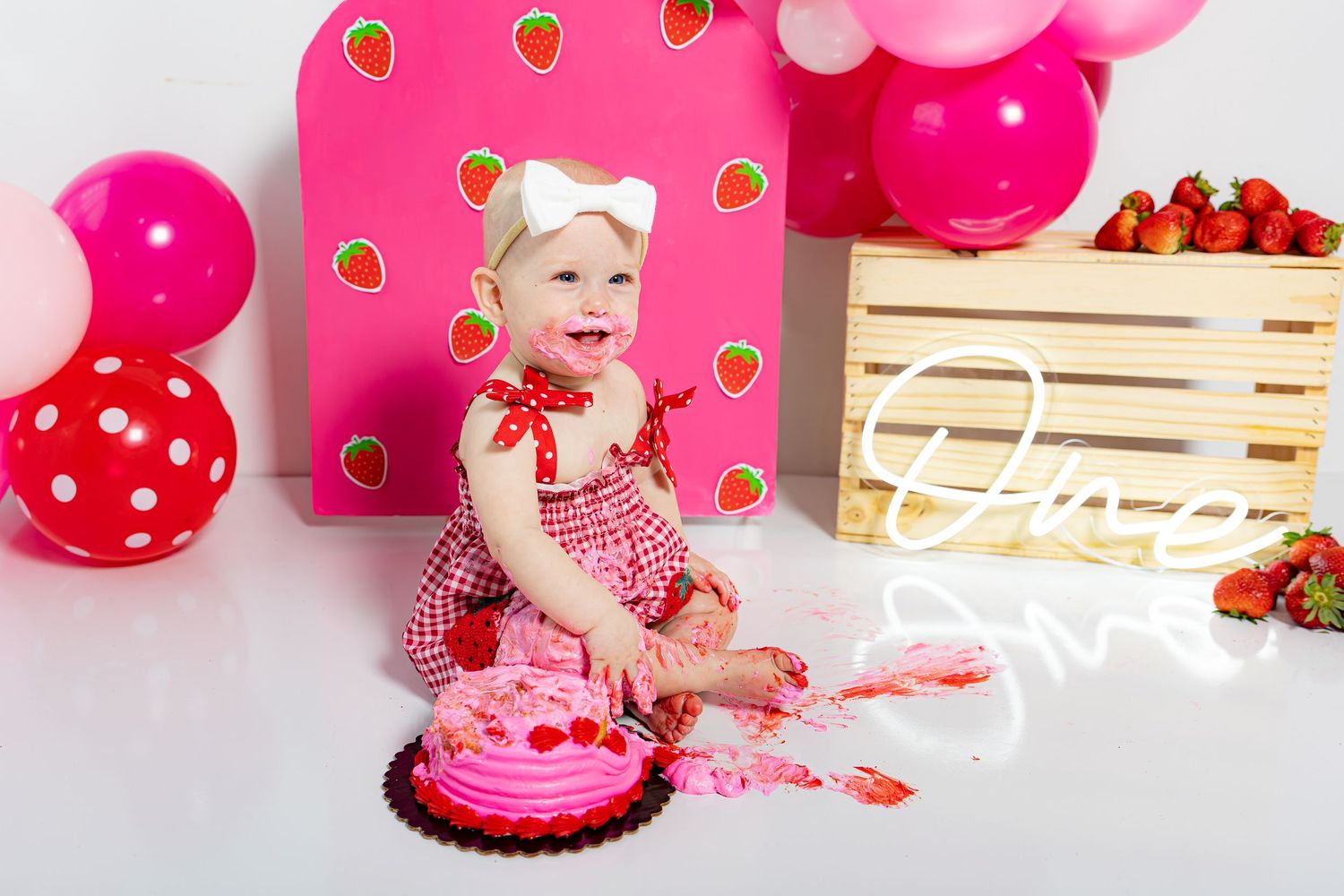 A pink and red themed cake smash photo session setup with wooden crates and polka dot decorations.