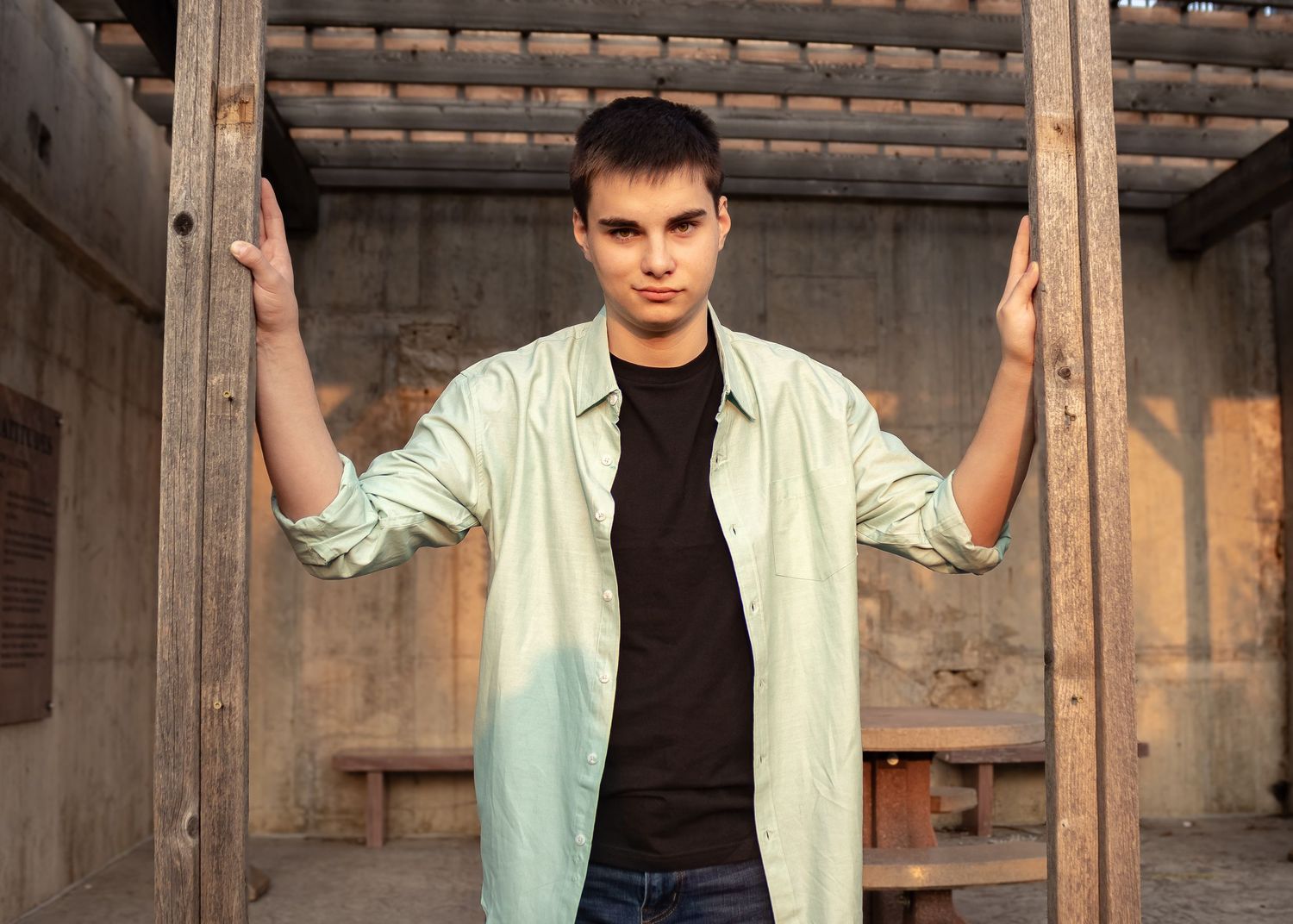 Person wearing a mint green button-down shirt and jeans poses against a rustic wooden wall background.