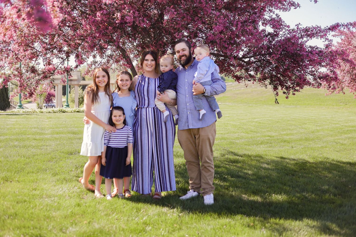 A family portrait taken outdoors with blooming cherry trees in the background.