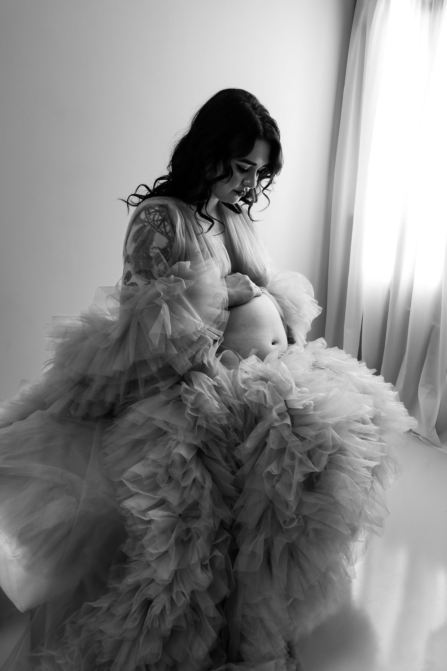A figure in a flowing gray tulle gown twirls gracefully in a bright room creating an ethereal artistic effect.