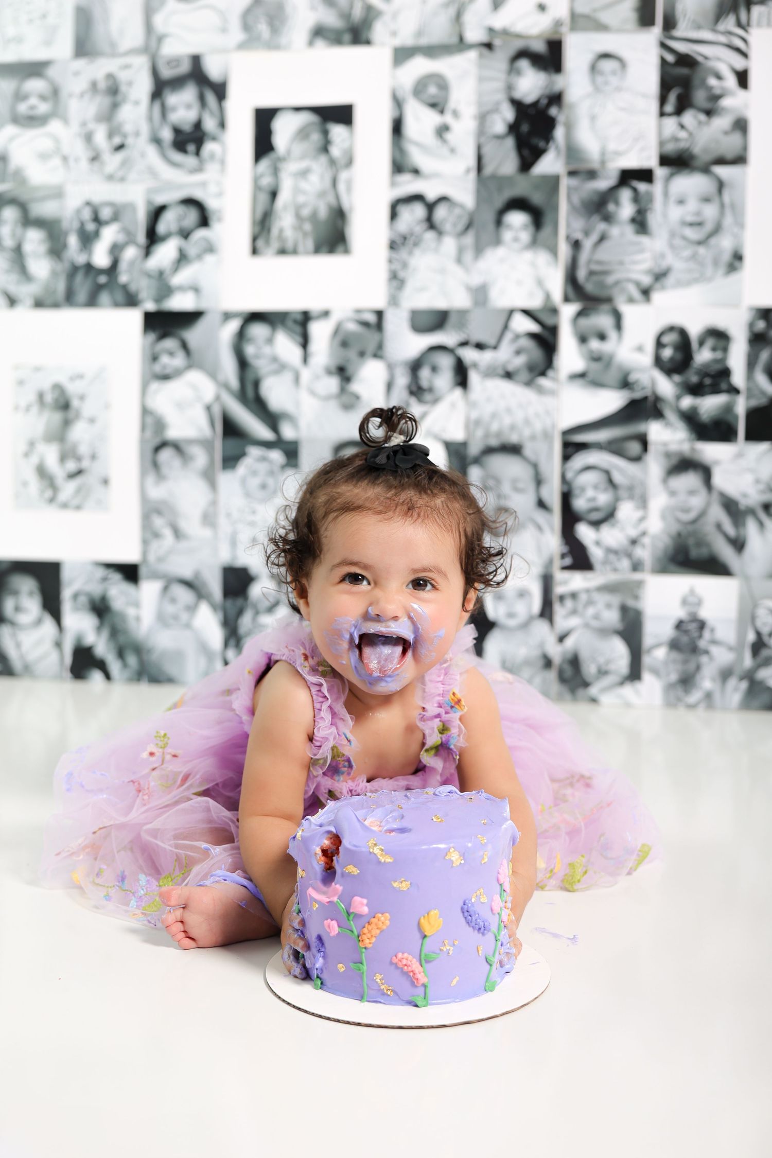 Baby with purple frosting on face laughs during cake smash photo session.