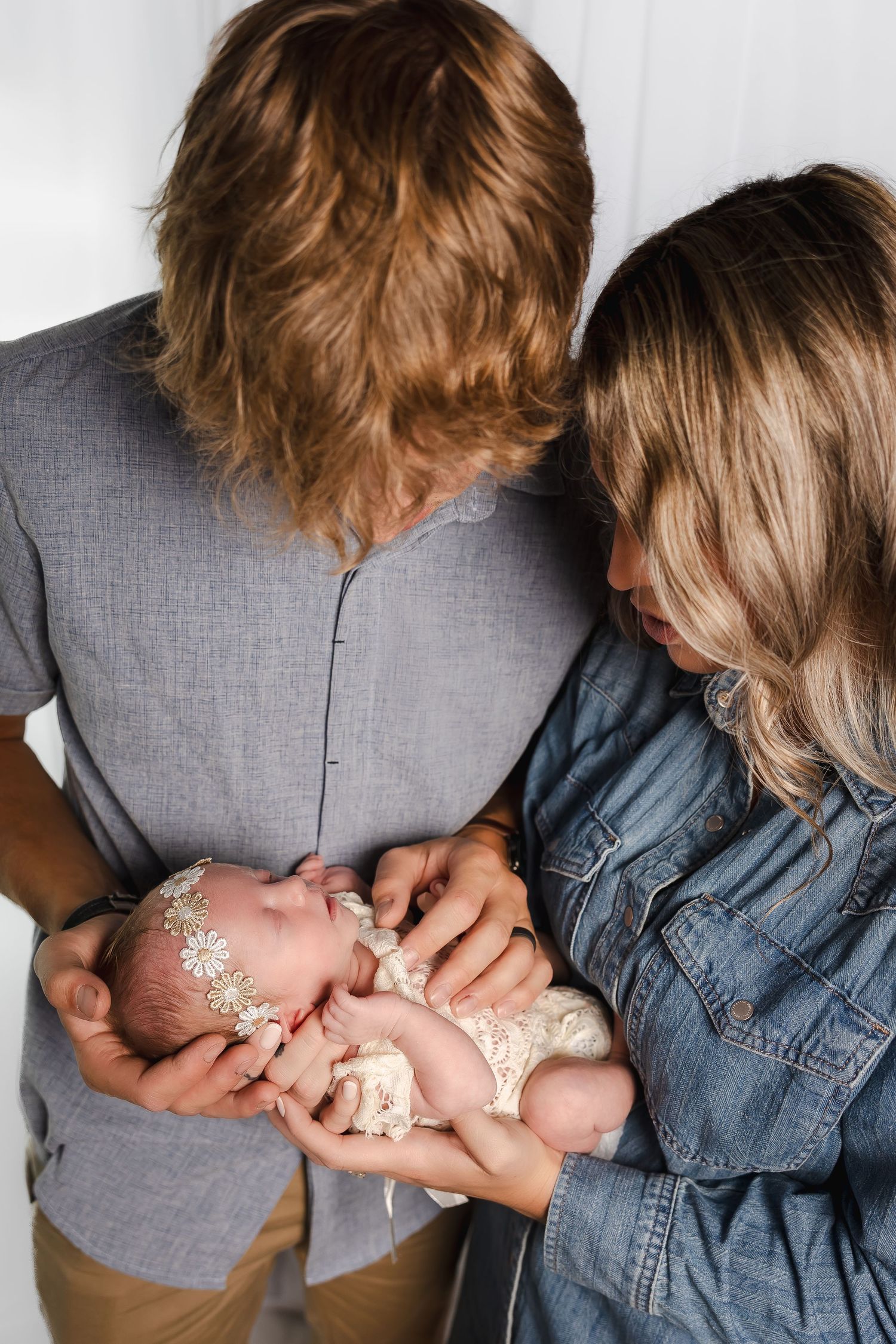 Parents in denim and grey clothing sharing intimate moment with their newborn.