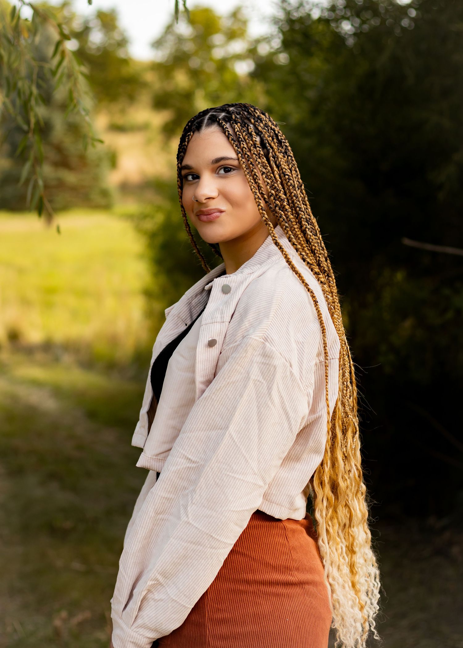 Outdoor portrait with willow trees featuring white jacket and rust-colored outfit.