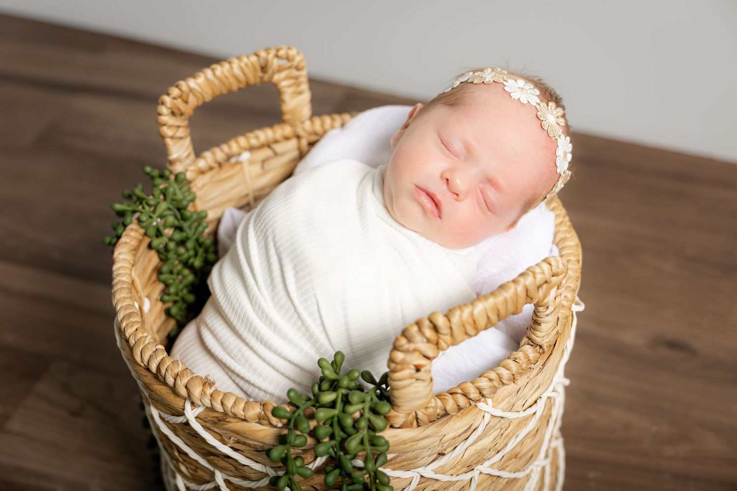 Sleeping newborn baby nestled in wicker basket with greenery accents.