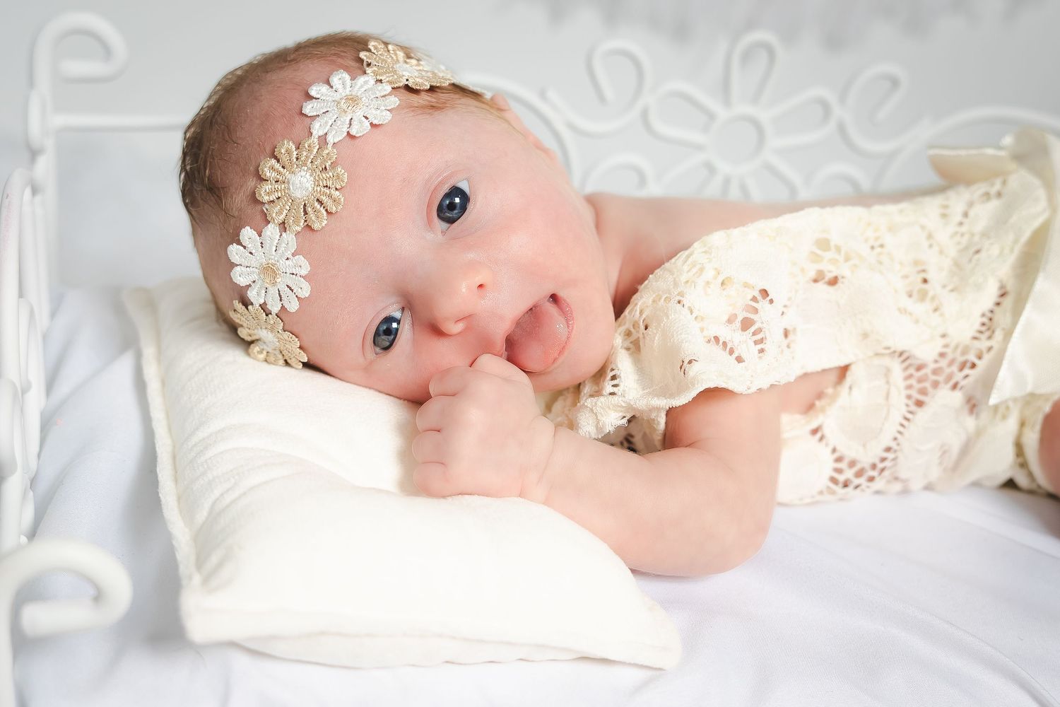 Newborn baby in cream lace outfit lying peacefully against white background.
