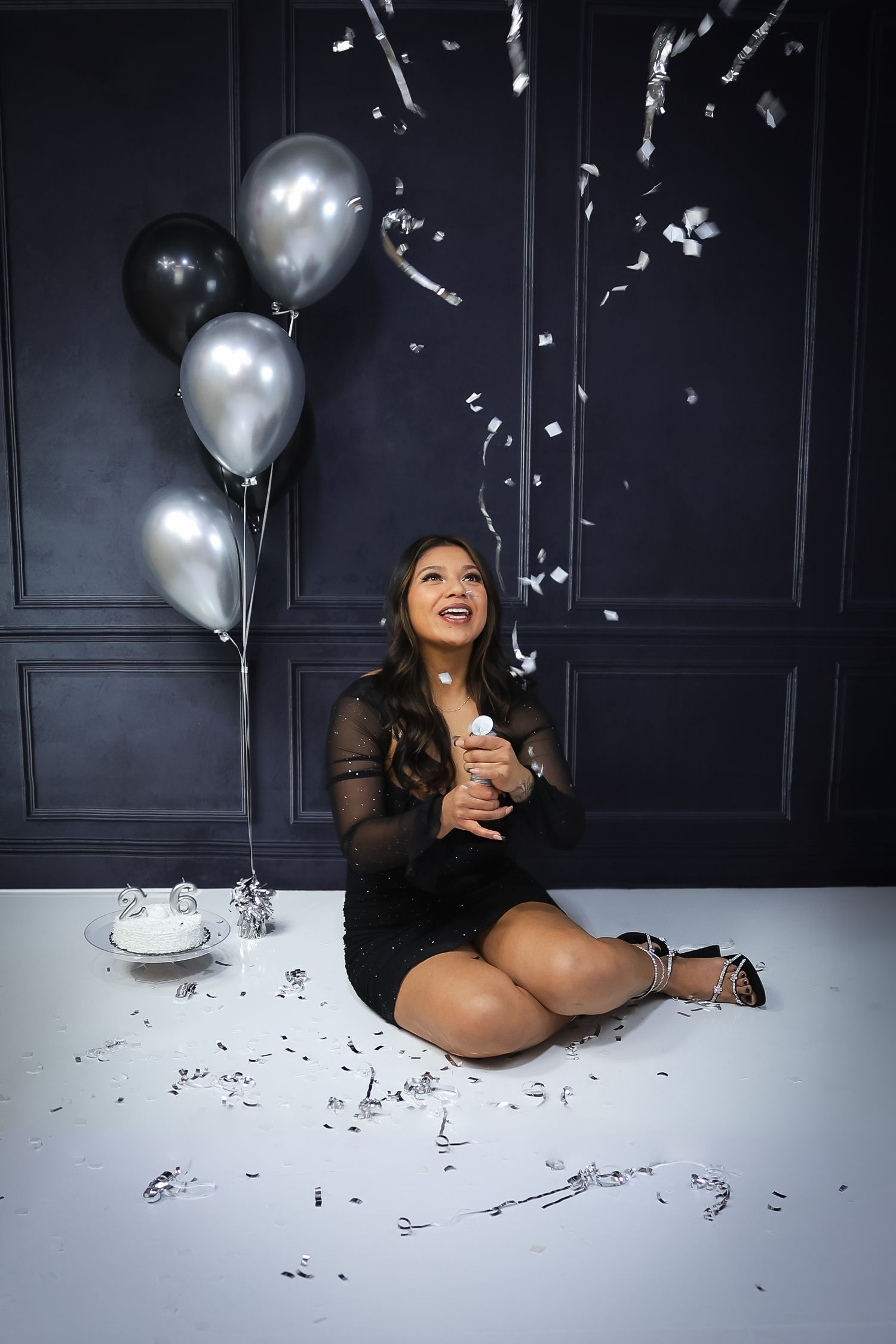 Celebratory photo shoot with silver balloons and confetti against dark wall.