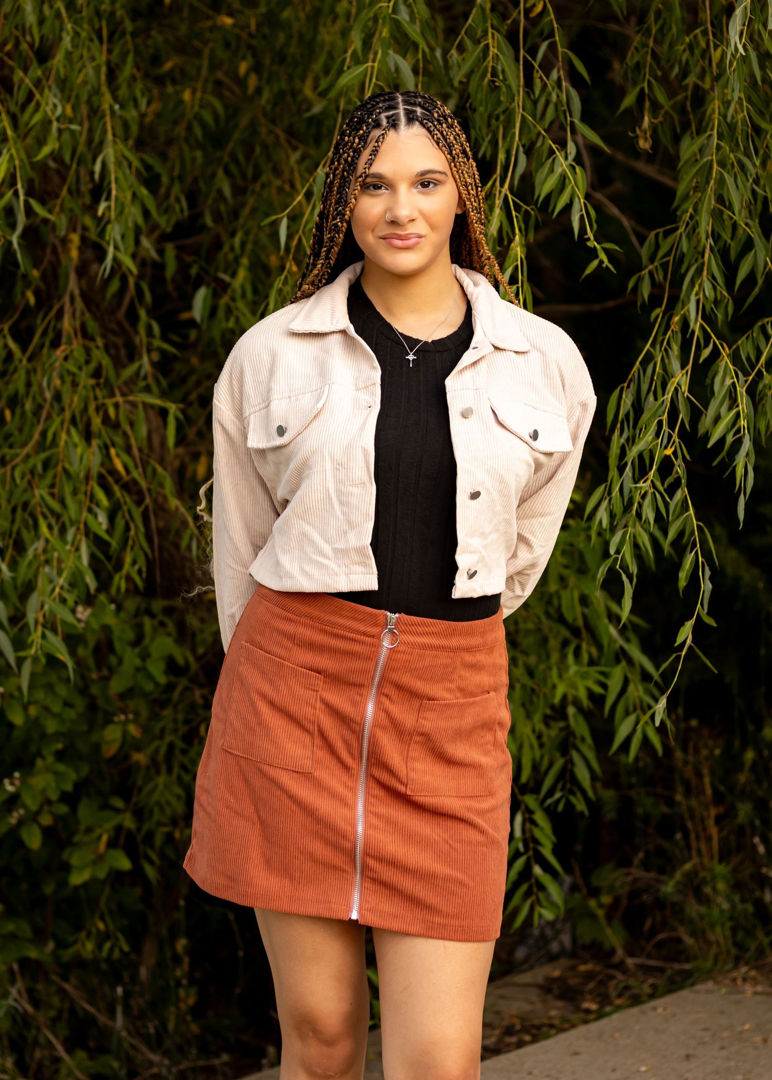 Casual outdoor fashion shoot with white jacket and rust-colored skirt against natural backdrop.