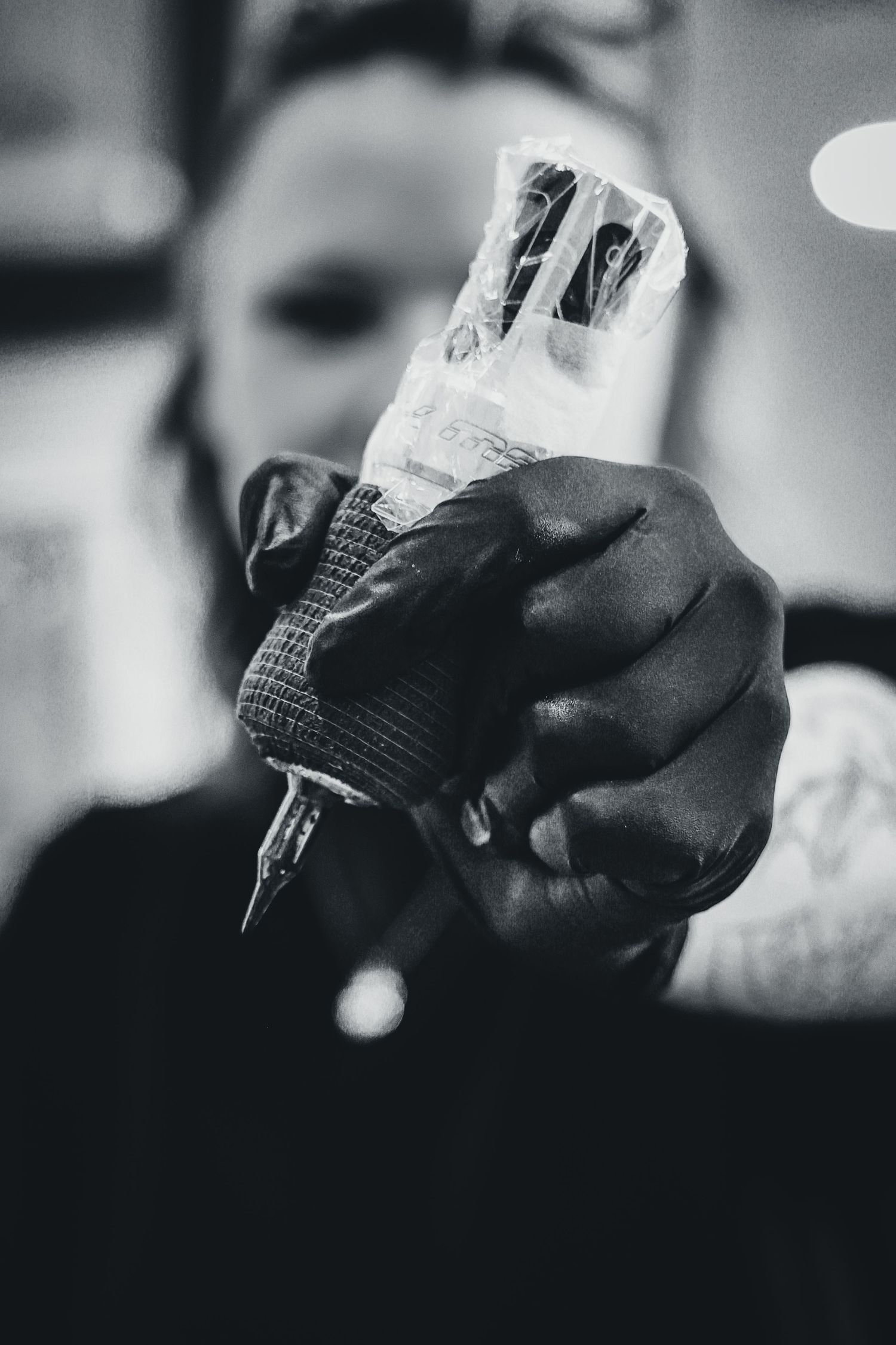 Black and white close-up of a tattoo artist holding a tattoo machine with gloved hand in a studio.