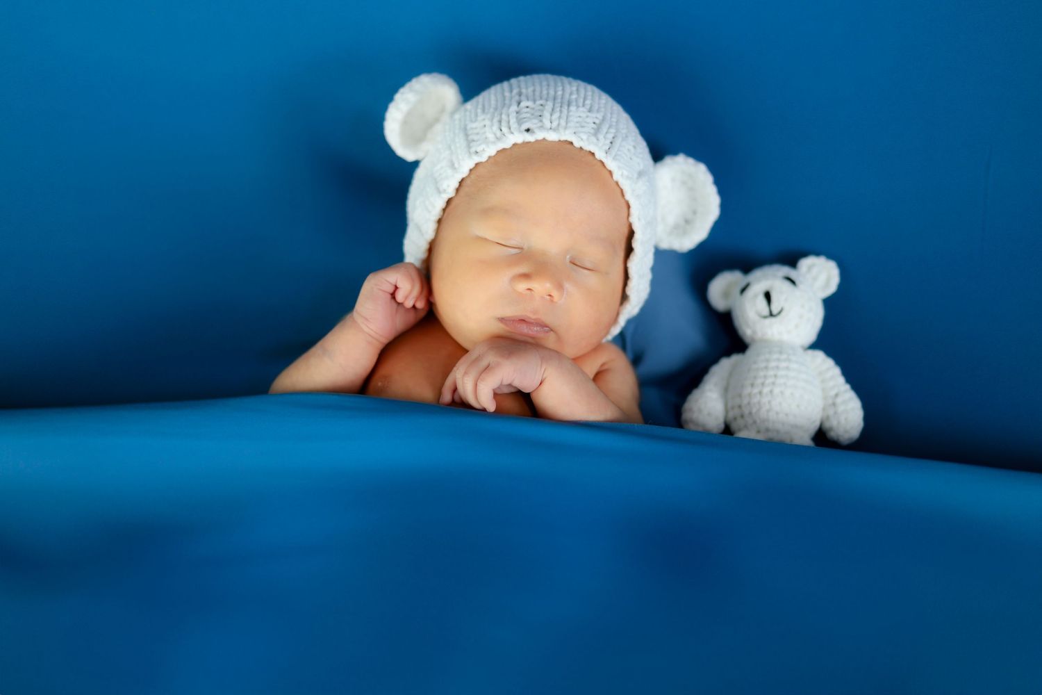 Sleeping newborn in blue setting with white plush toy companion.