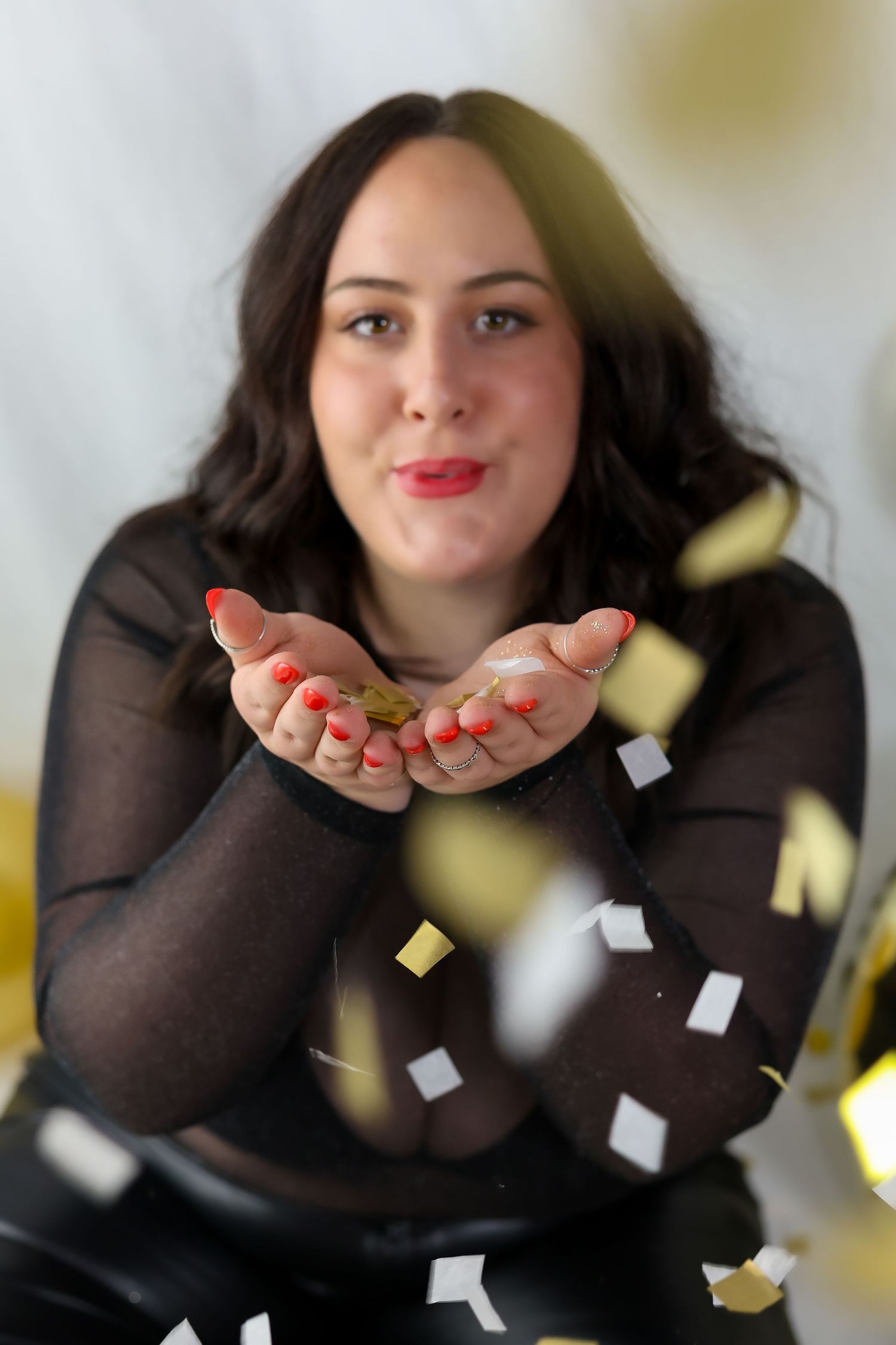 Confetti being blown from cupped hands while wearing a black top against a light background.