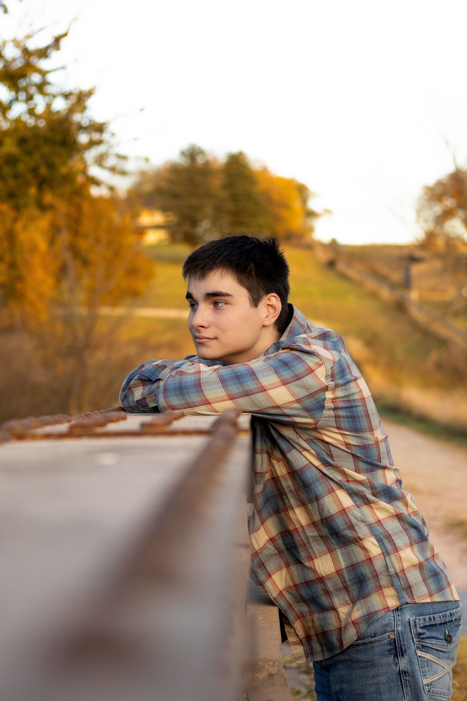 A person in plaid leans thoughtfully on a railing during golden hour.