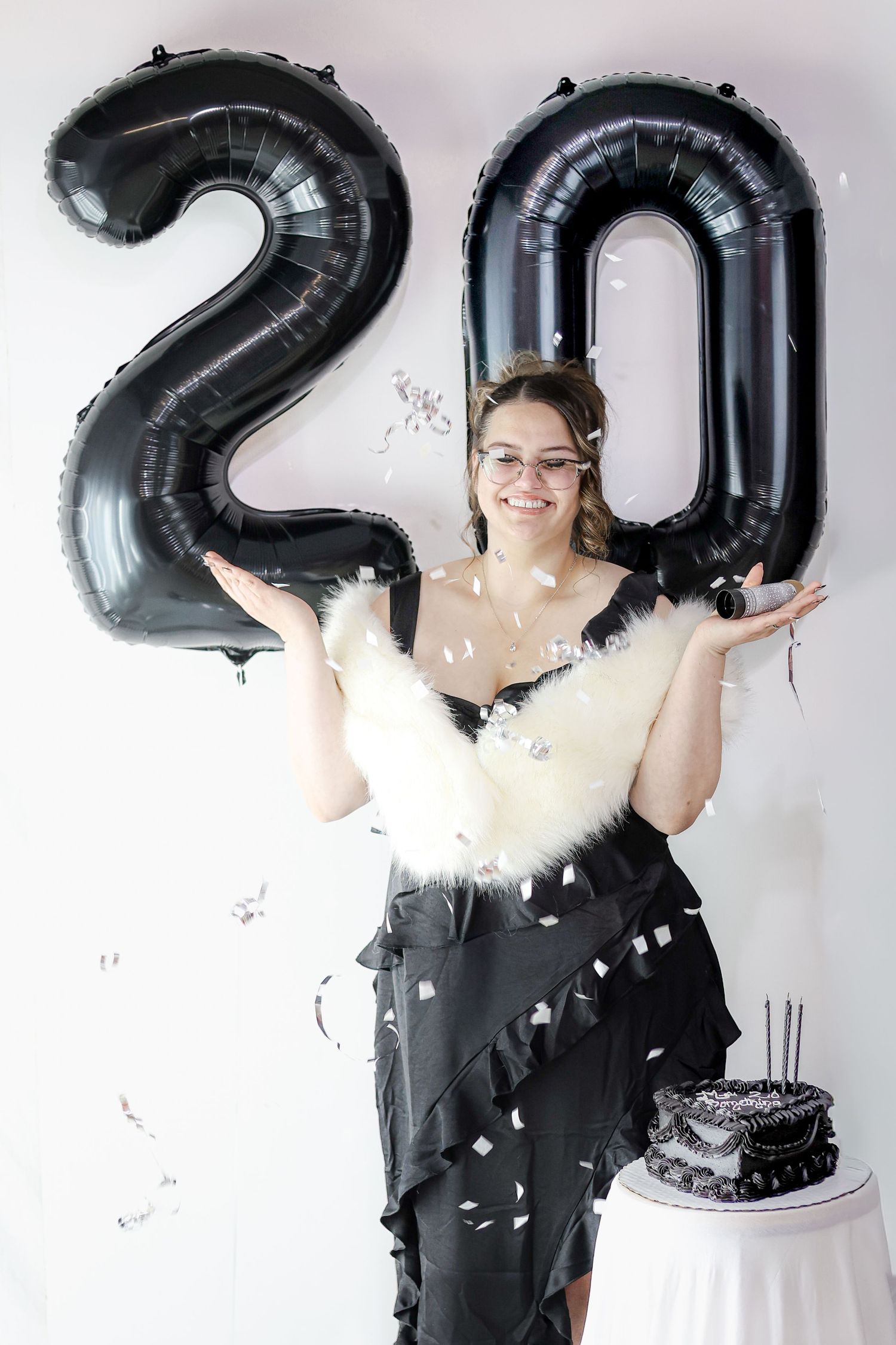 A celebration photoshoot with black number balloons and confetti against a white backdrop.