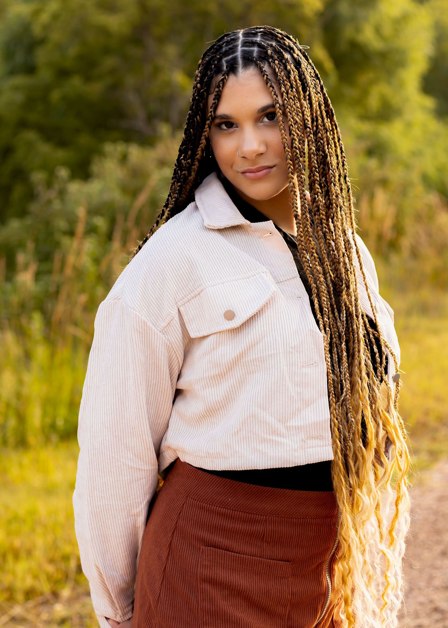A person wearing a white corduroy jacket poses against a golden autumn background.