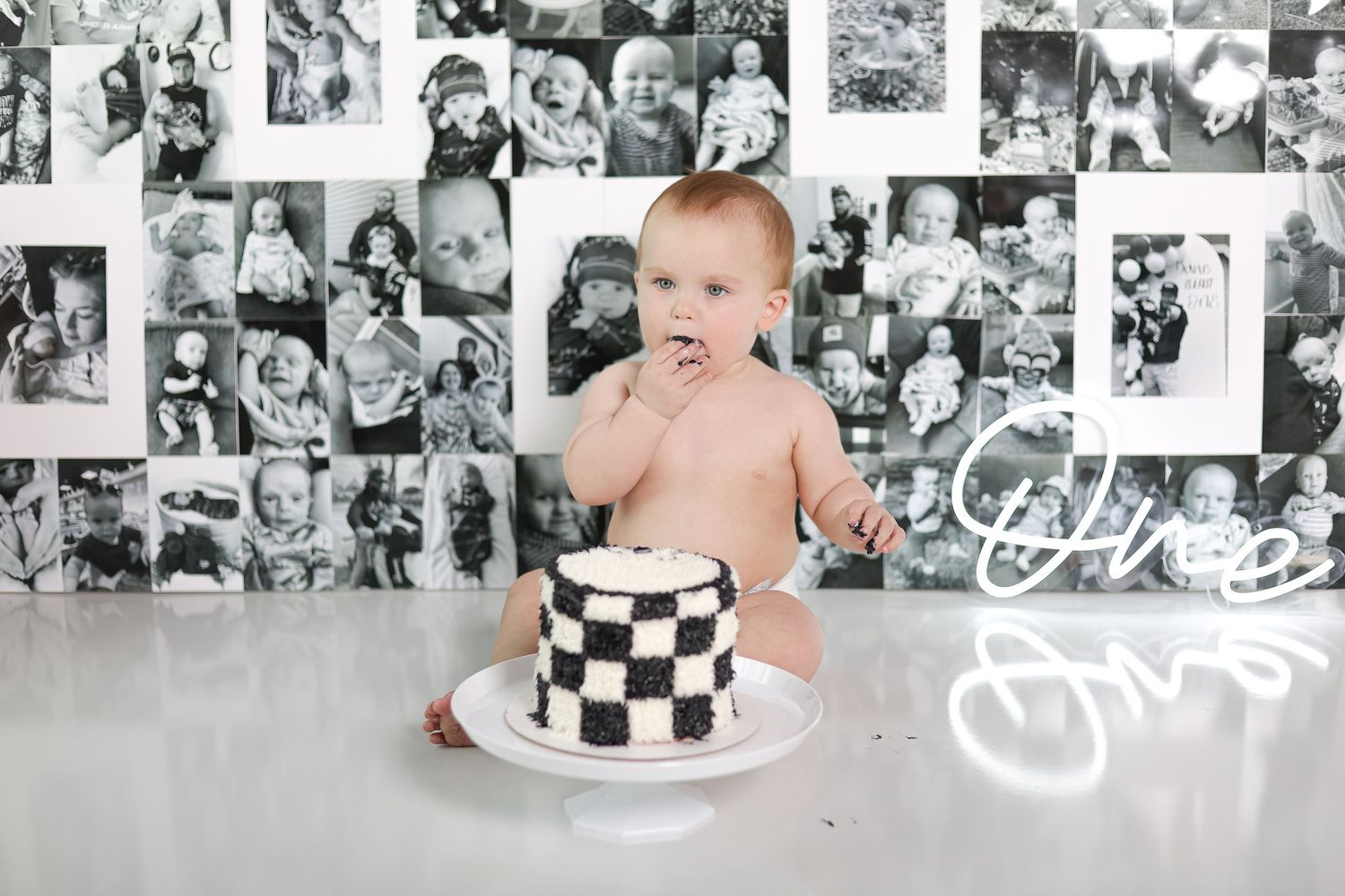 A baby sits with a black and white checkered cake during a cake smash photoshoot.