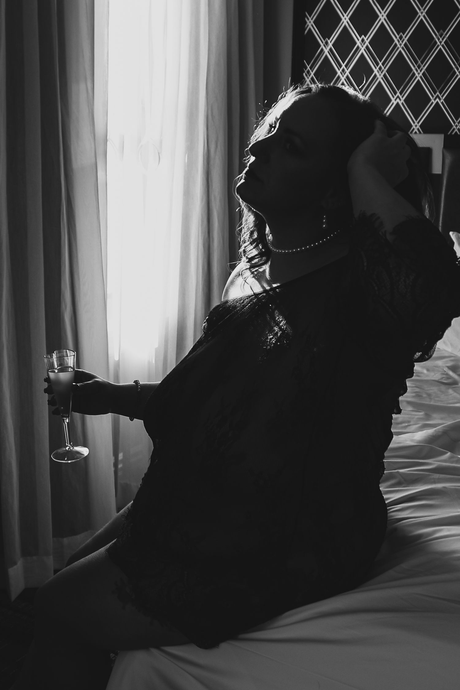 Artistic black and white silhouettes of a figure reclining on a bed against a window with diamond pattern.