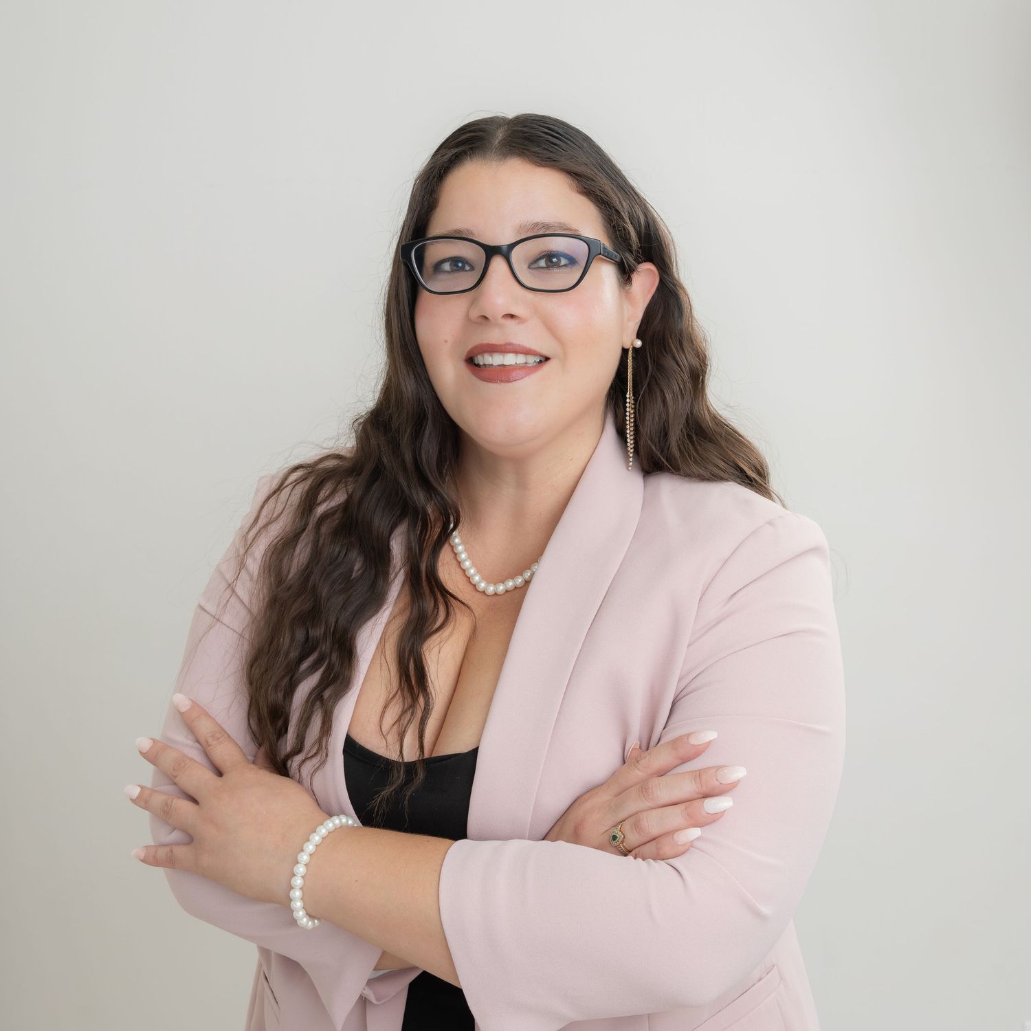 Professional wearing a light pink blazer and glasses poses confidently against a white background.