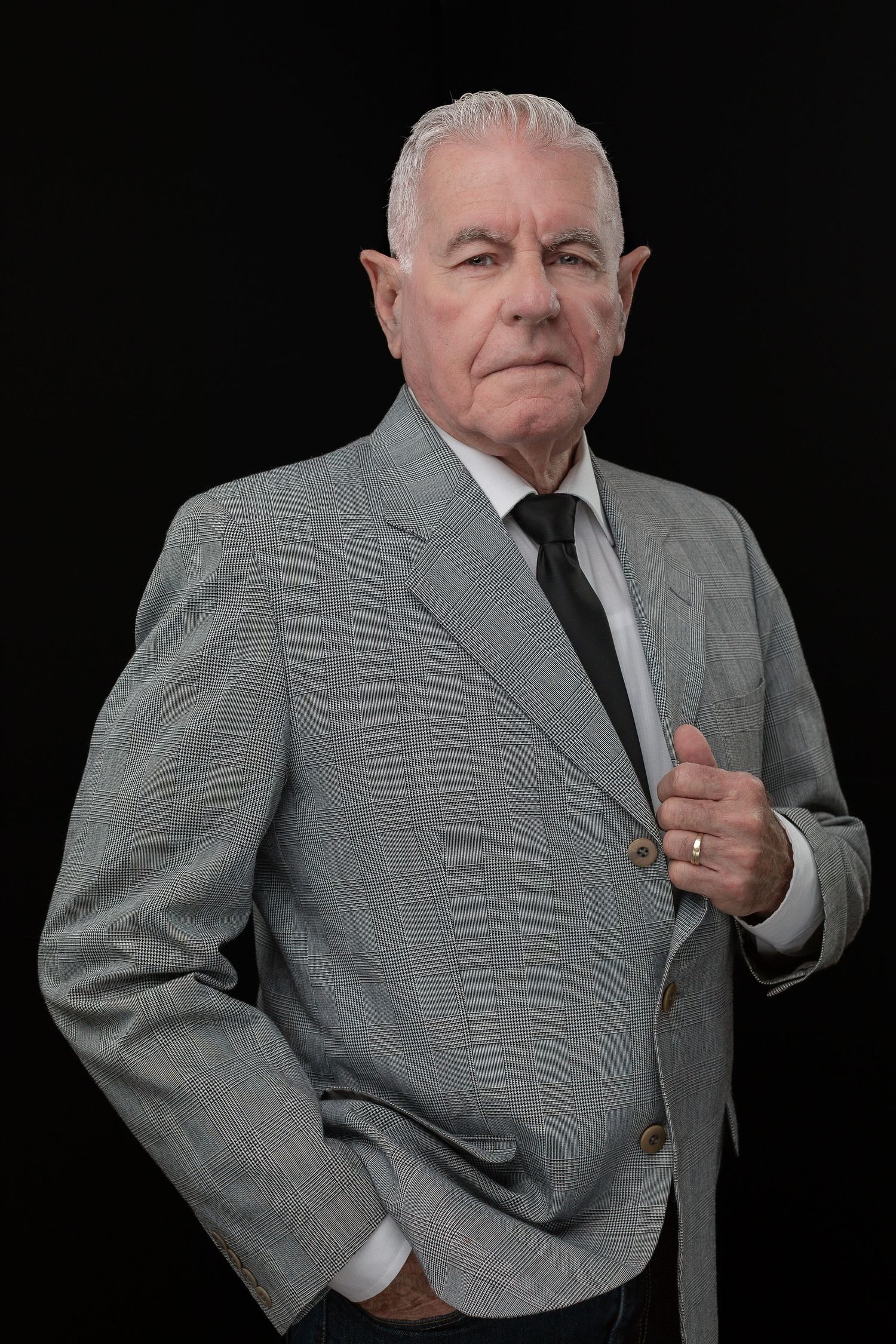 Distinguished gentleman in grey suit and tie poses professionally against black backdrop.