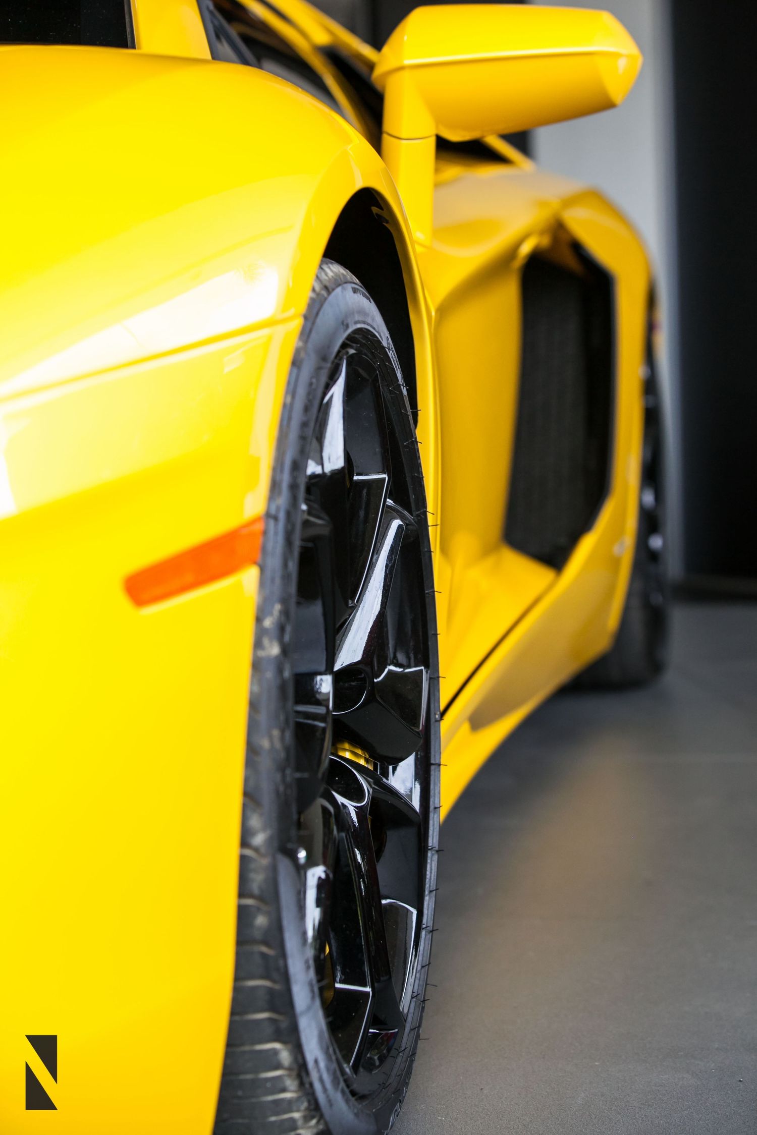 Close-up view of a bright yellow sports car showing black alloy wheel and aerodynamic side panel details.