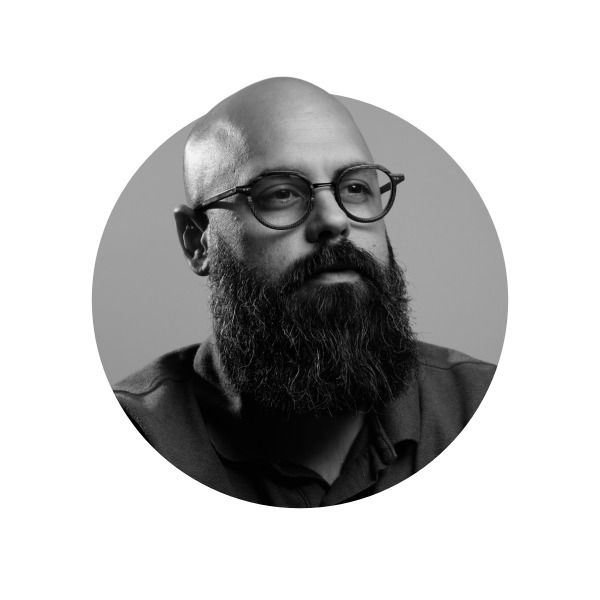 Black and white portrait of a bald man with a thick beard and glasses, looking thoughtfully to the side.