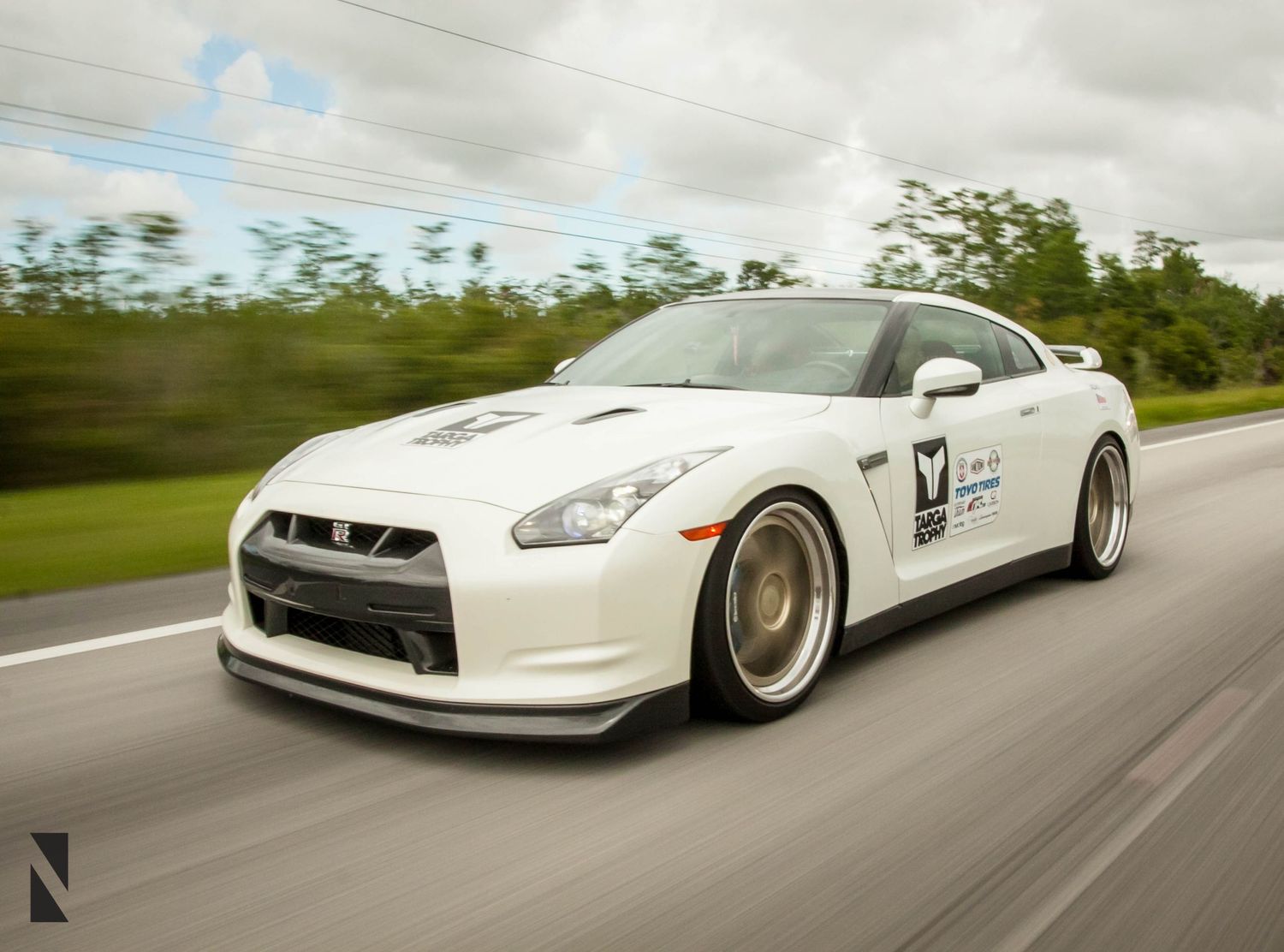 White Nissan GT-R sports car speeding down a highway with gold rims and racing decals.