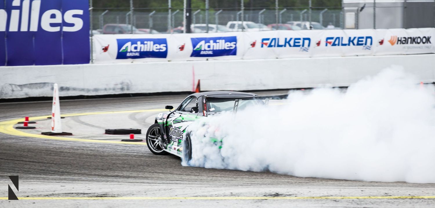 Drift car creates huge cloud of white smoke while sliding sideways on racetrack with Falken advertising banners.