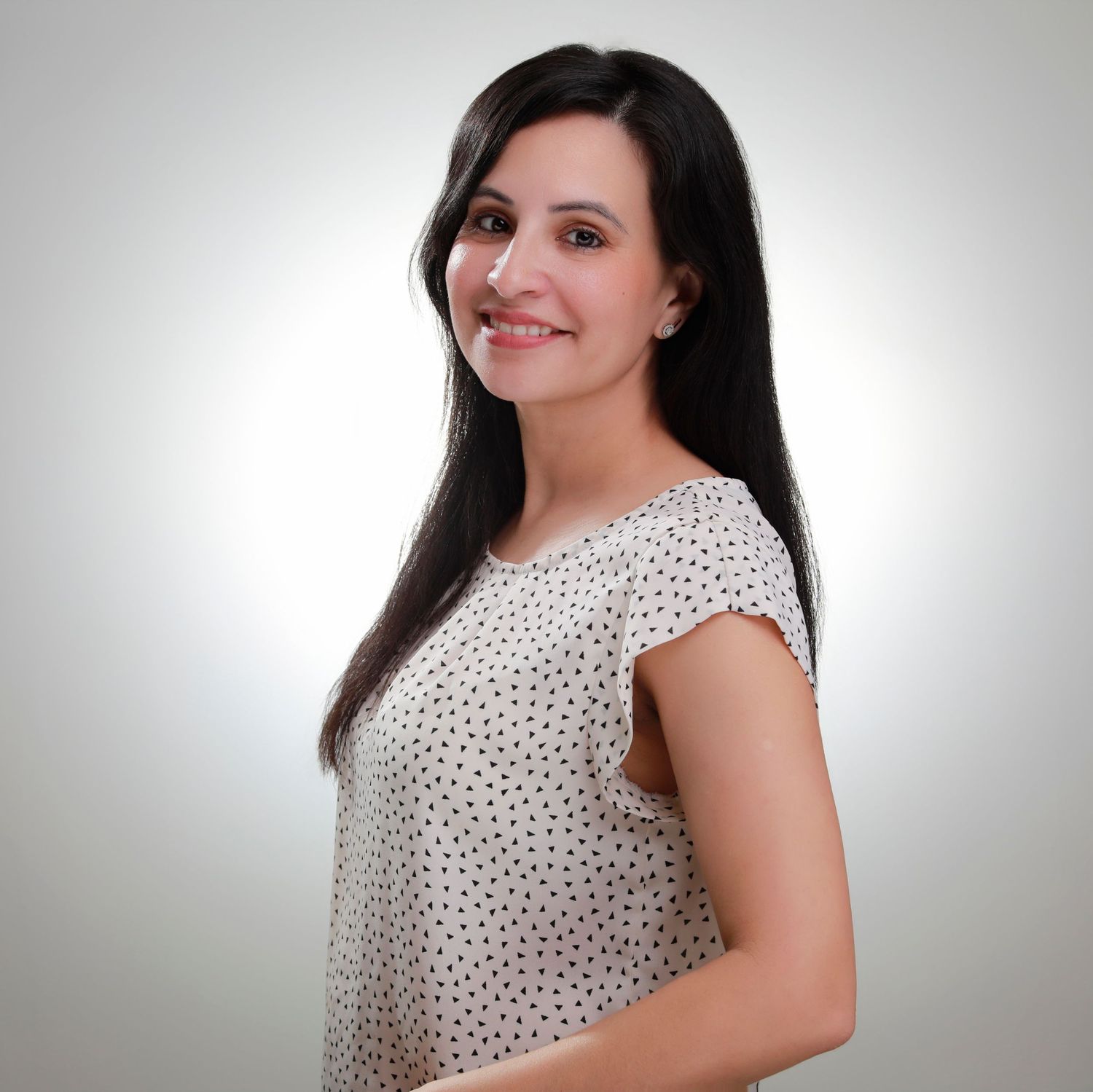 Professional portrait of a woman with long dark hair wearing a polka dot blouse against a light background.