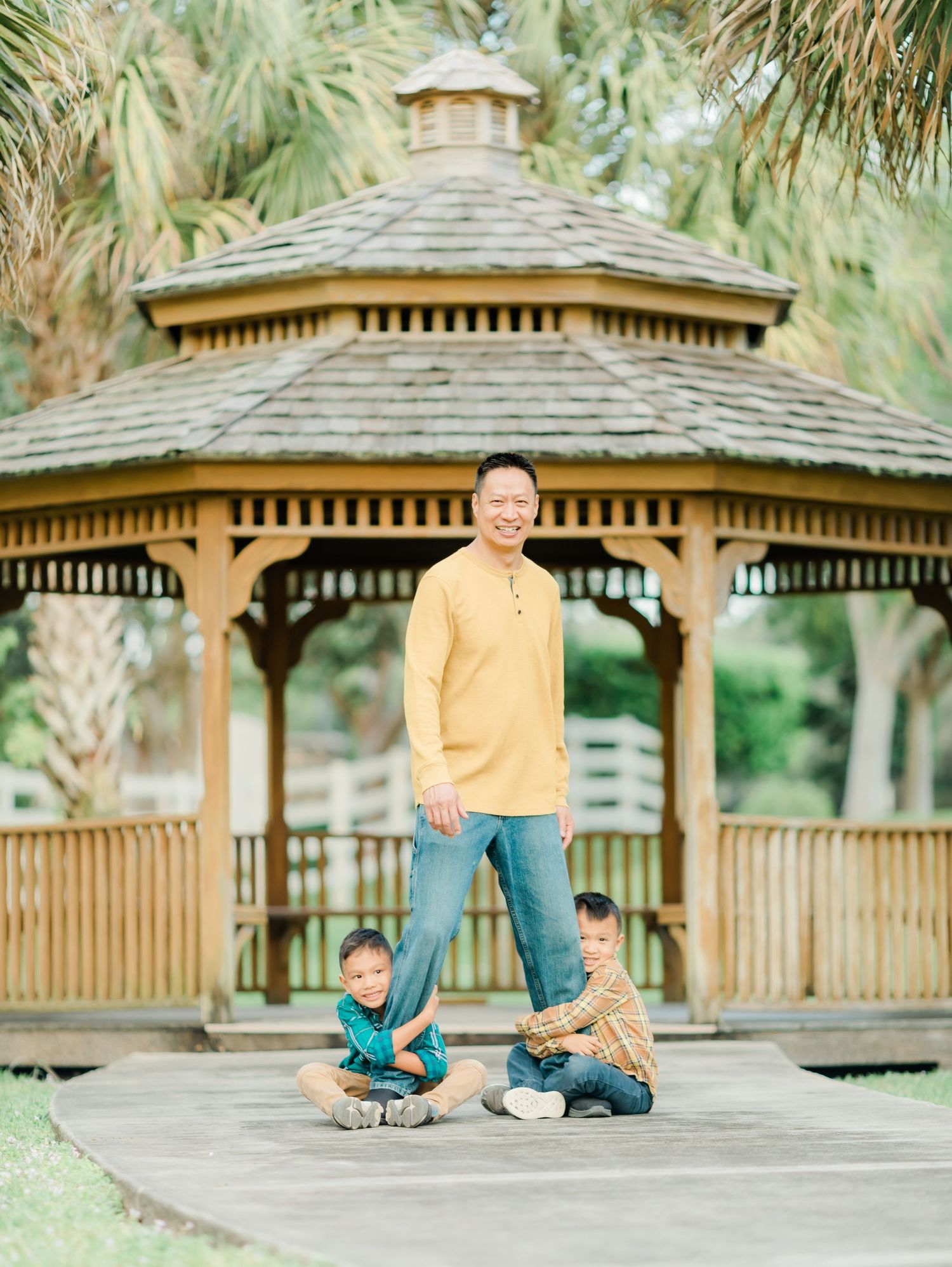 A family poses playfully by a wooden gazebo surrounded by palm trees.