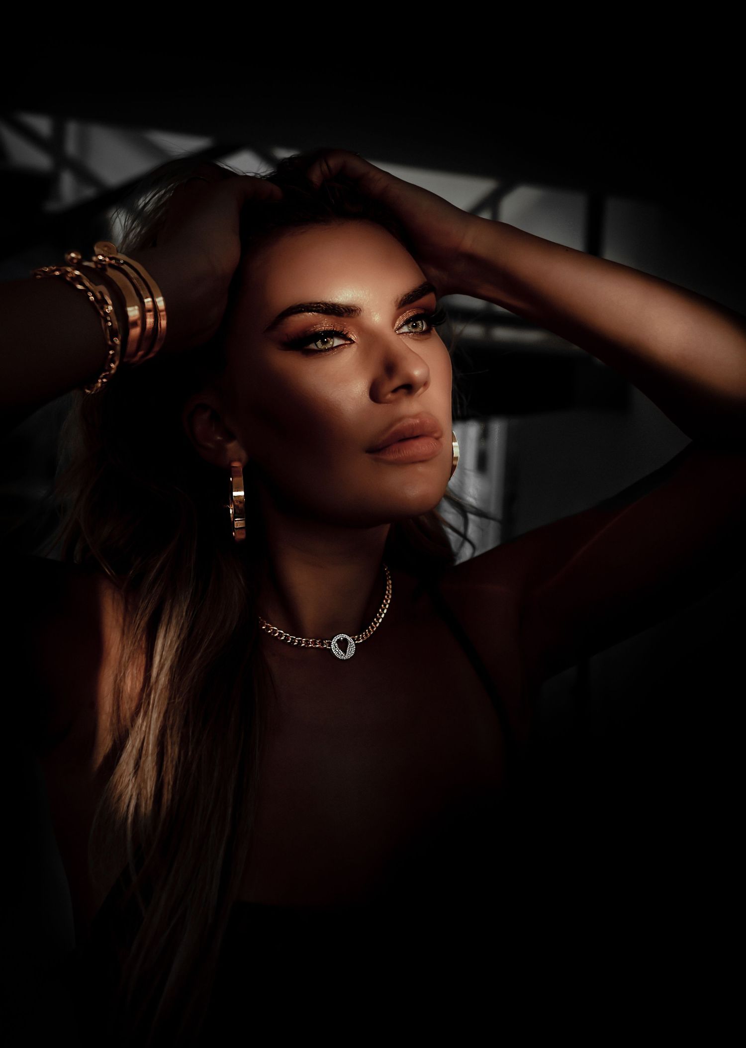 Moody portrait in shadows with jewelry and dramatic lighting.
