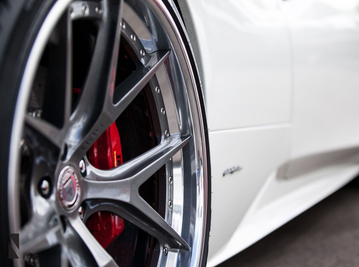 Close-up detail shot of a sports car's alloy wheel with red brake caliper visible behind silver spokes.