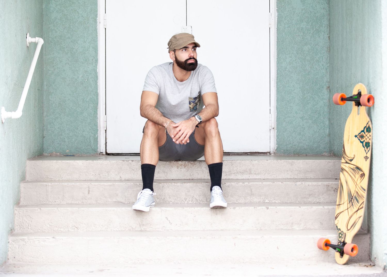 A person in a gray t-shirt and shorts sits on concrete steps with a skateboard visible in the corner.