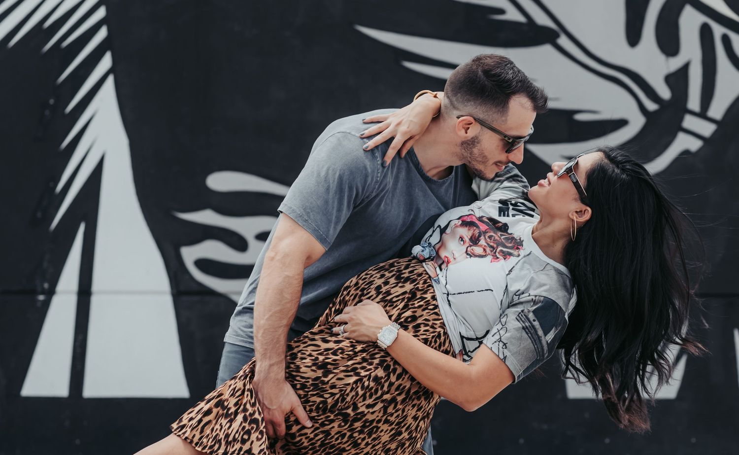A couple performs a romantic dip pose against a black and white mural background.