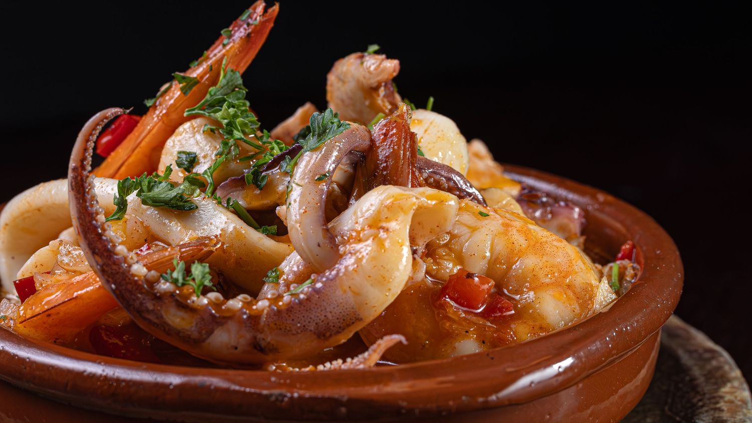 A clay dish filled with grilled seafood including octopus, shrimp and calamari garnished with fresh herbs.