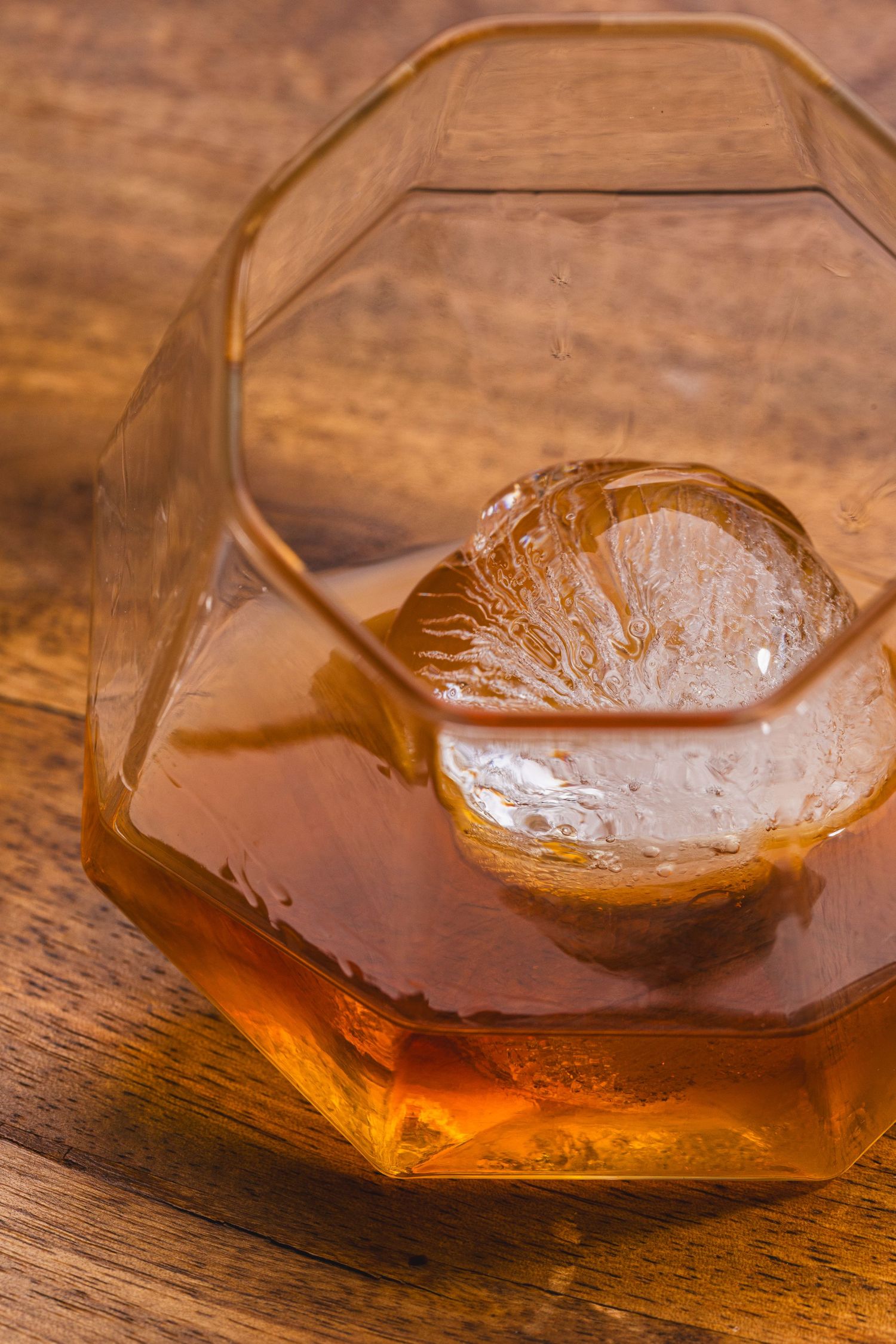 A close-up sequence showing whiskey swirling in a faceted glass tumbler on a wooden surface with melting ice cube.