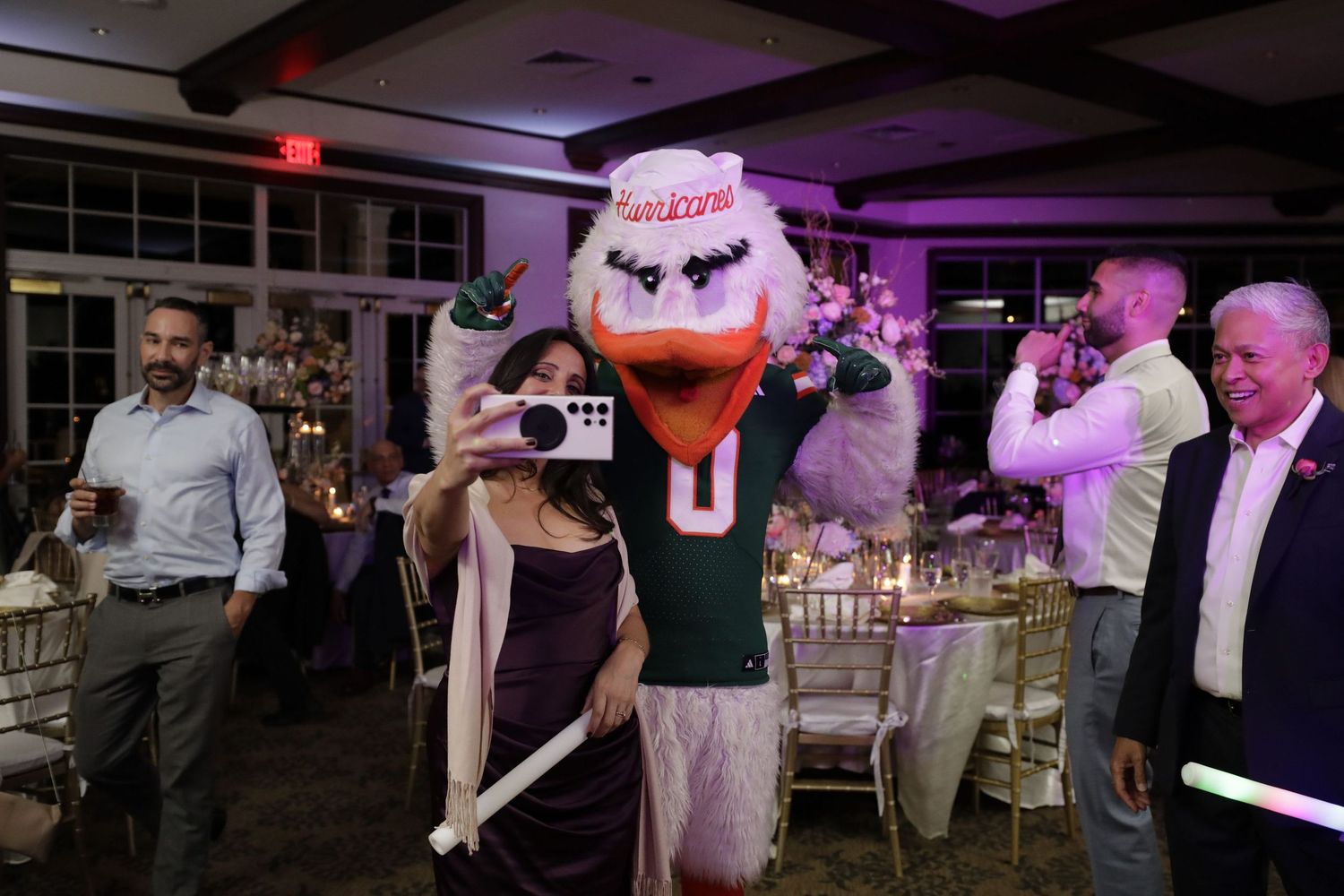 Sebastian the Ibis mascot entertains guests at an evening reception with purple lighting in an indoor venue.