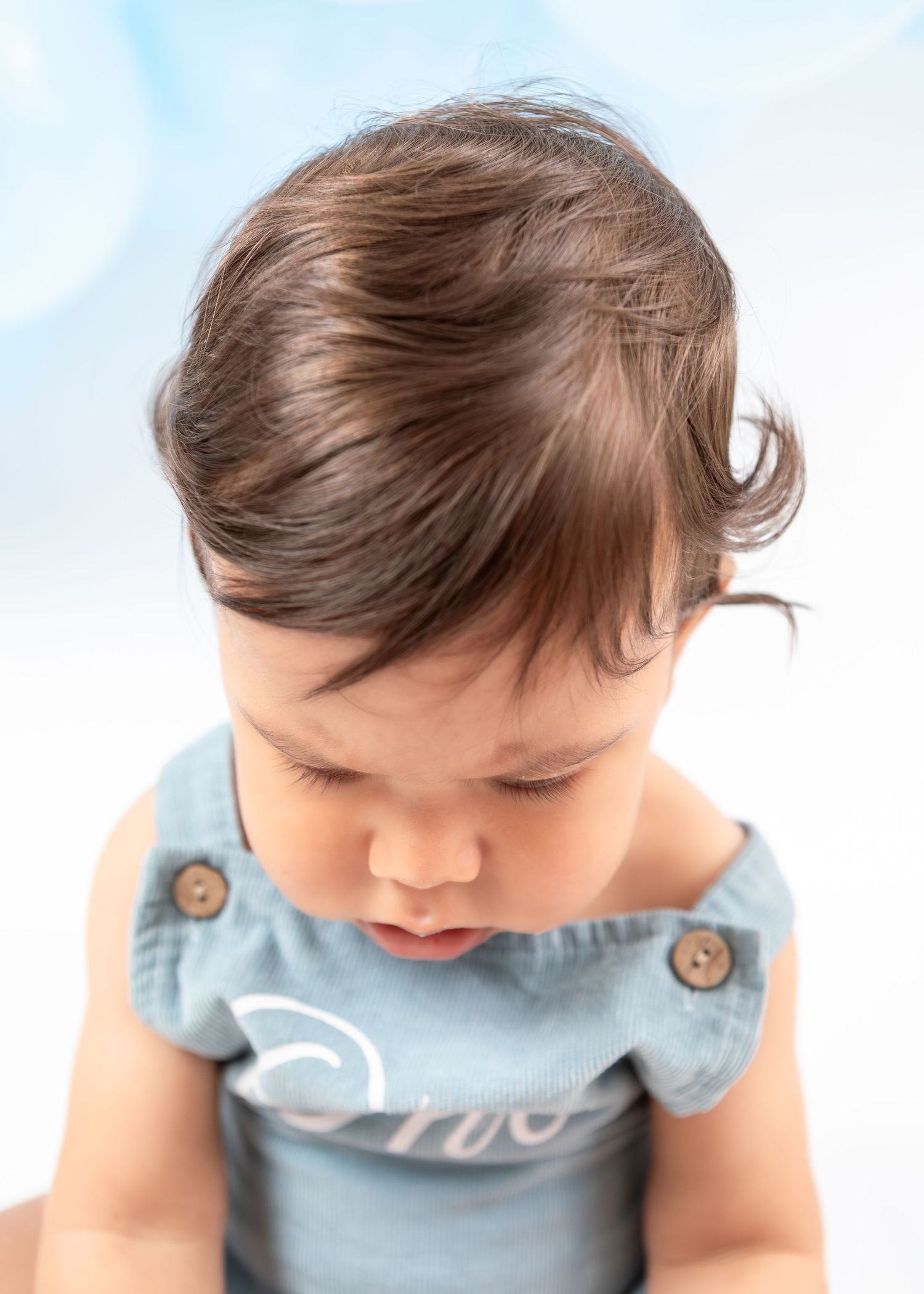 Close up portrait showing soft brown hair and blue romper with 'One' text.