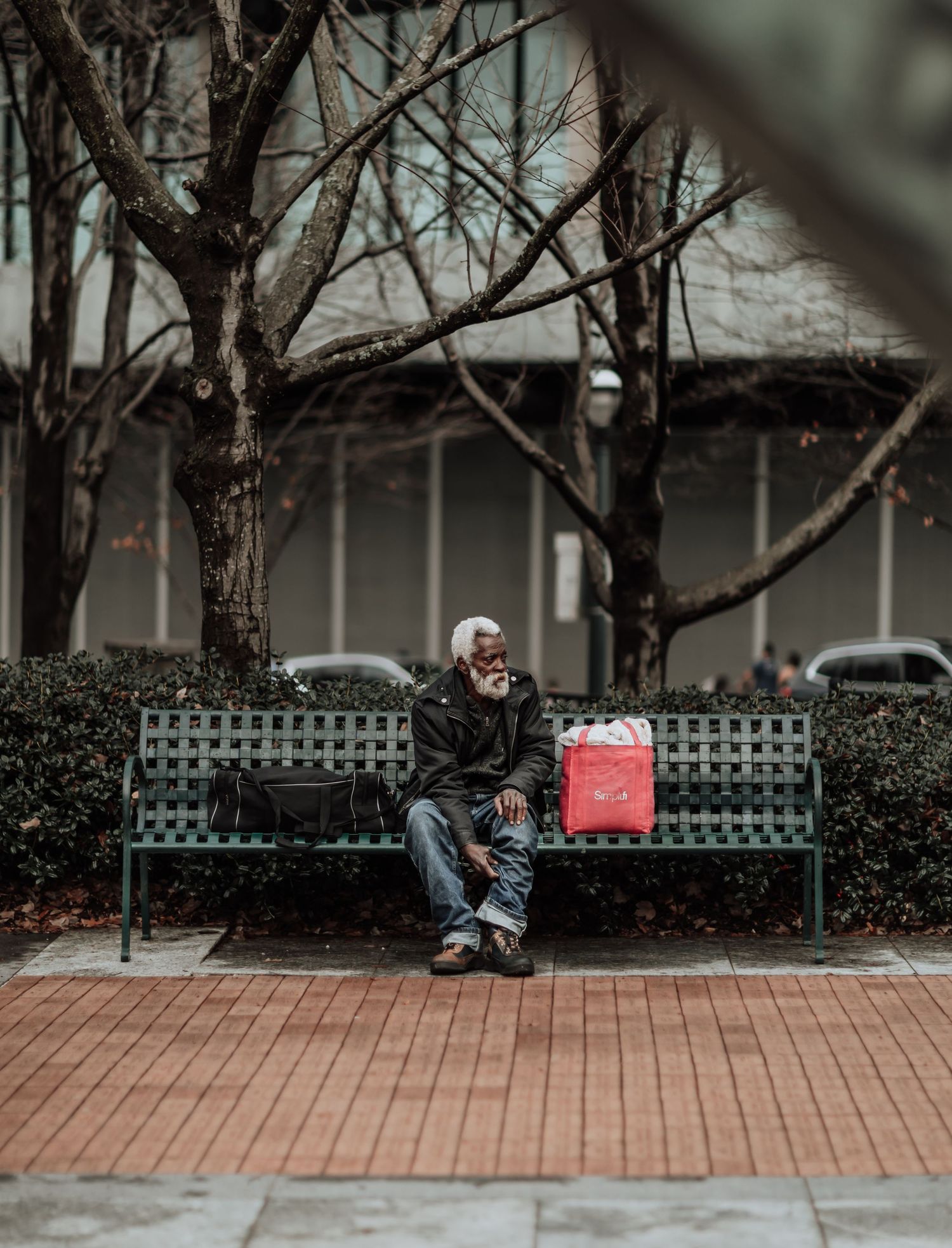 Person sitting alone on green bench with shopping bag in winter setting.