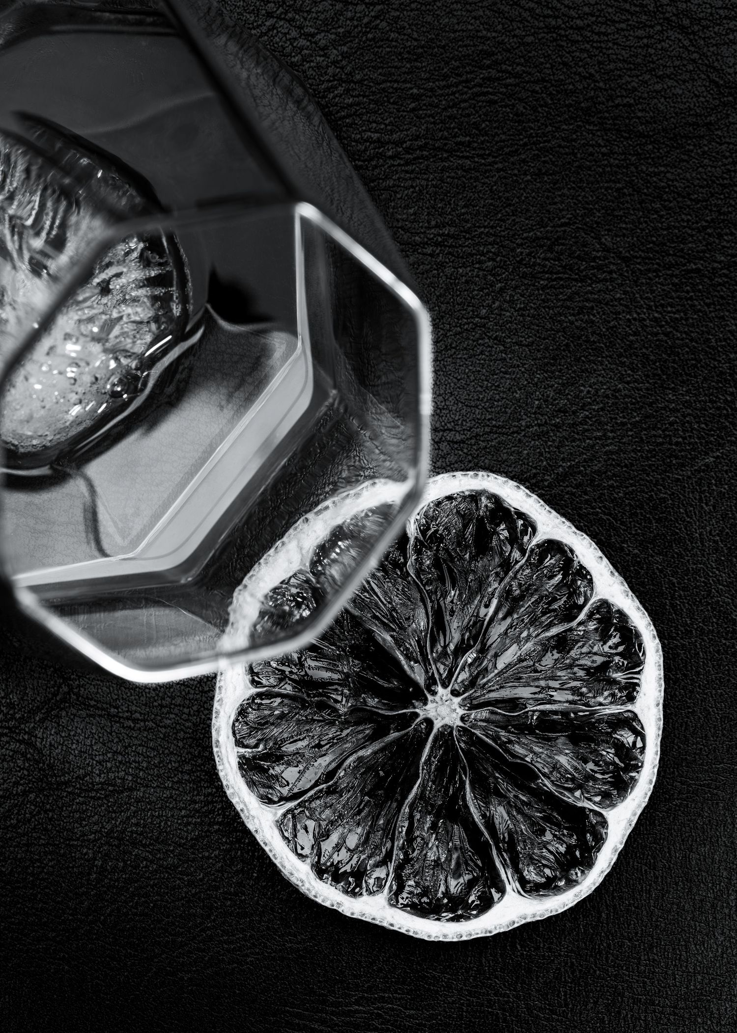 A black and white shot of a citrus slice with dramatic shadows and sharp detail against a dark background.