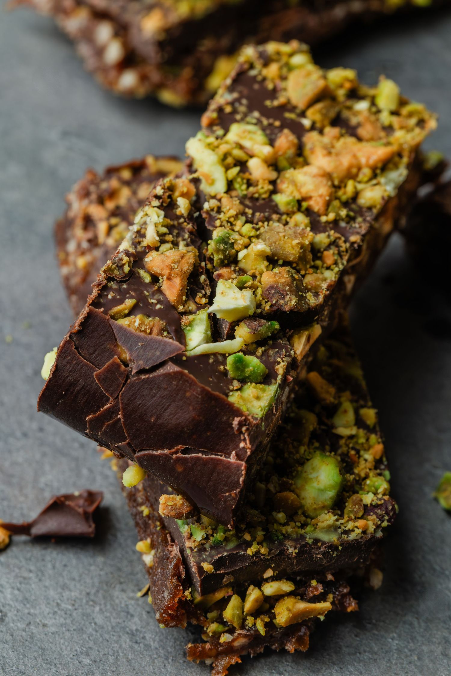 Close-up shots of dark chocolate bark with crushed pistachios and nuts arranged on a gray slate surface.