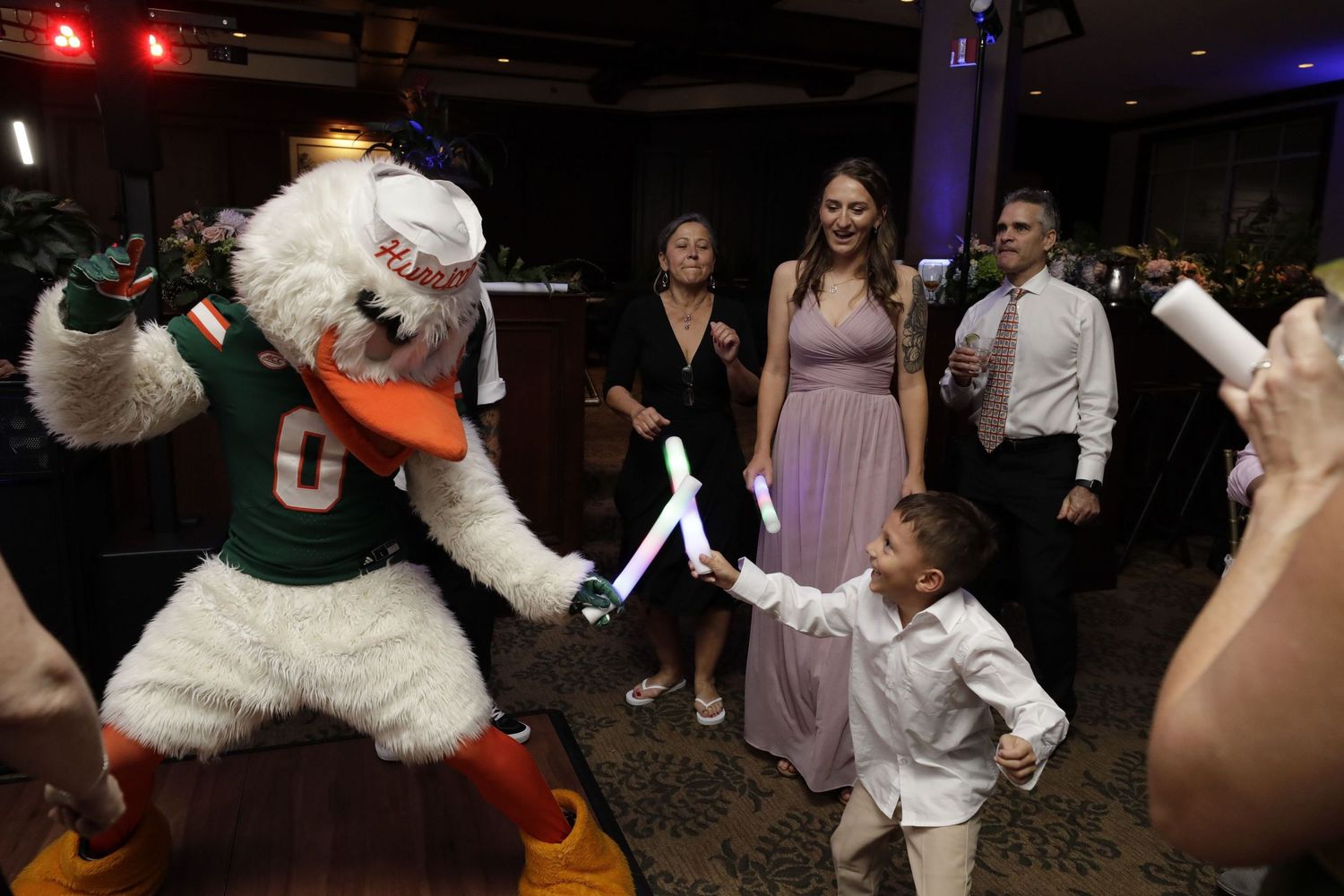 Miami Hurricanes mascot Sebastian the Ibis dances with a young child at what appears to be a party or celebration event.