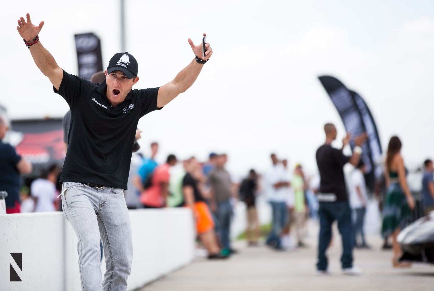 Enthusiastic person in black shirt and light pants celebrating with arms raised at outdoor event.