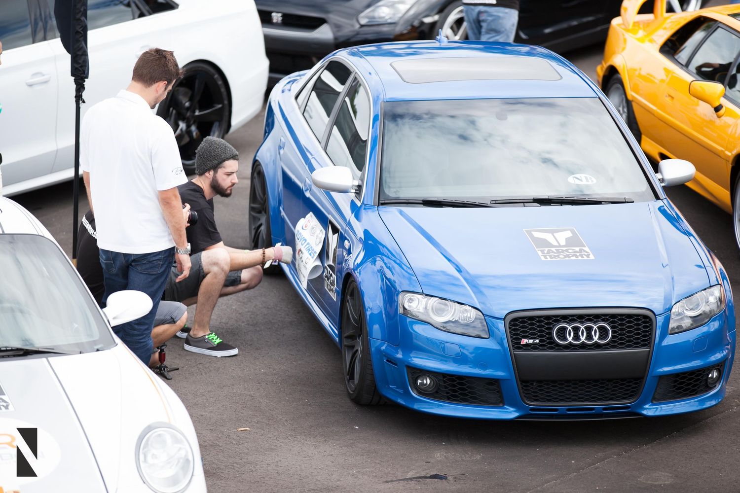 A bright blue Audi being inspected in a parking lot with other vehicles visible.