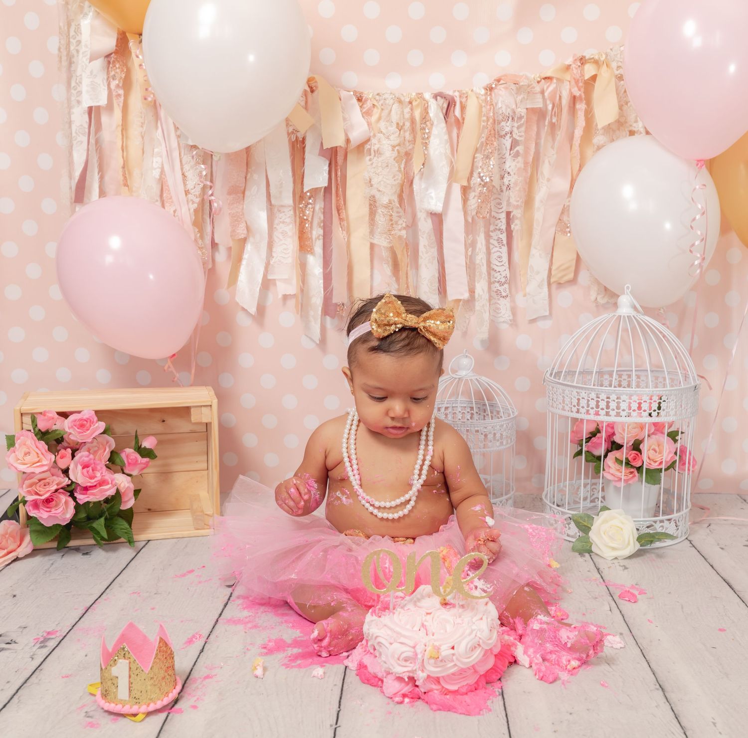 Baby in pink tutu and pearls celebrates first birthday with cake smash photo shoot and pink party decorations.