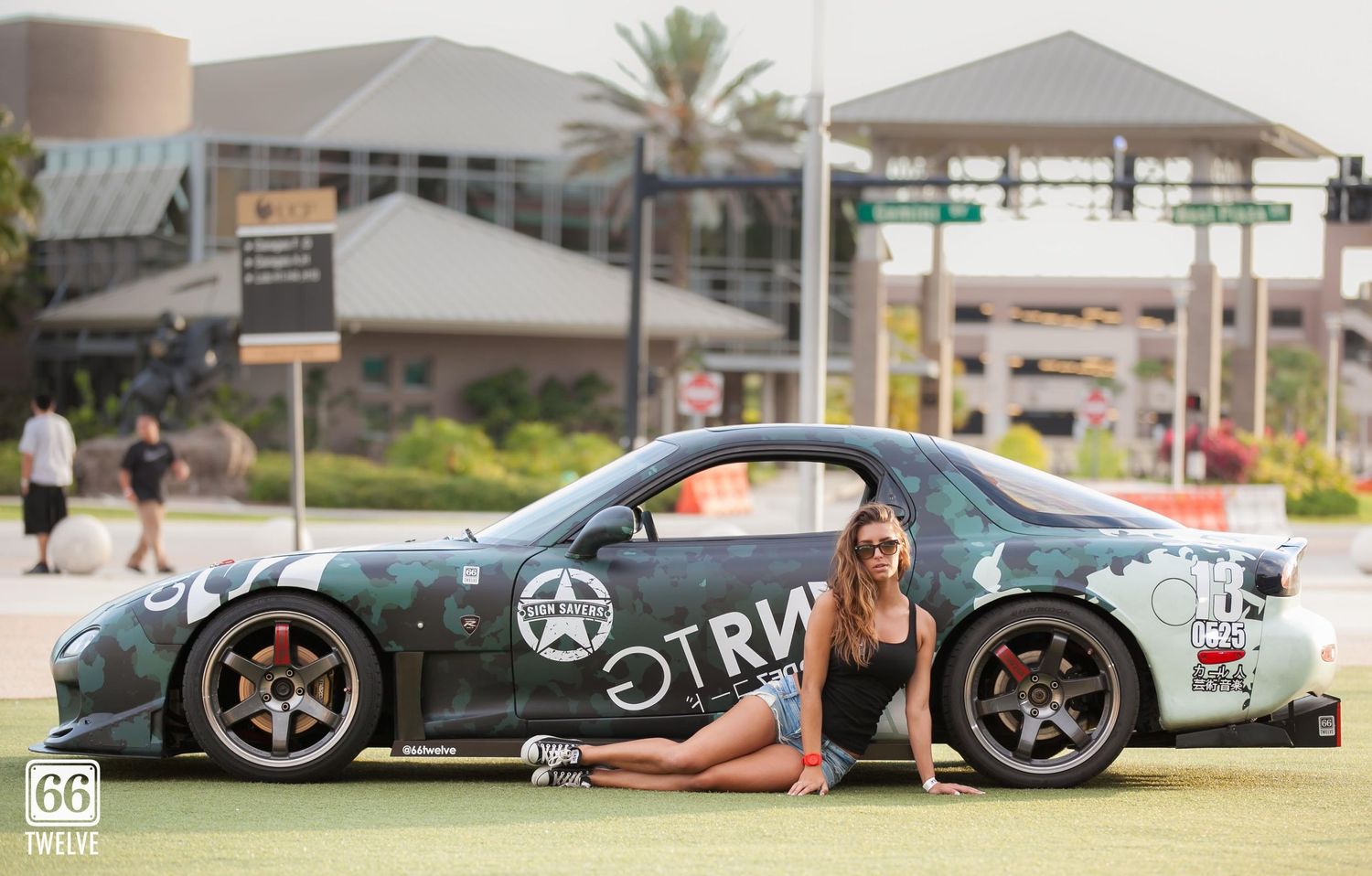 Modified sports car with racing graphics displayed outdoors with modern architecture in background.