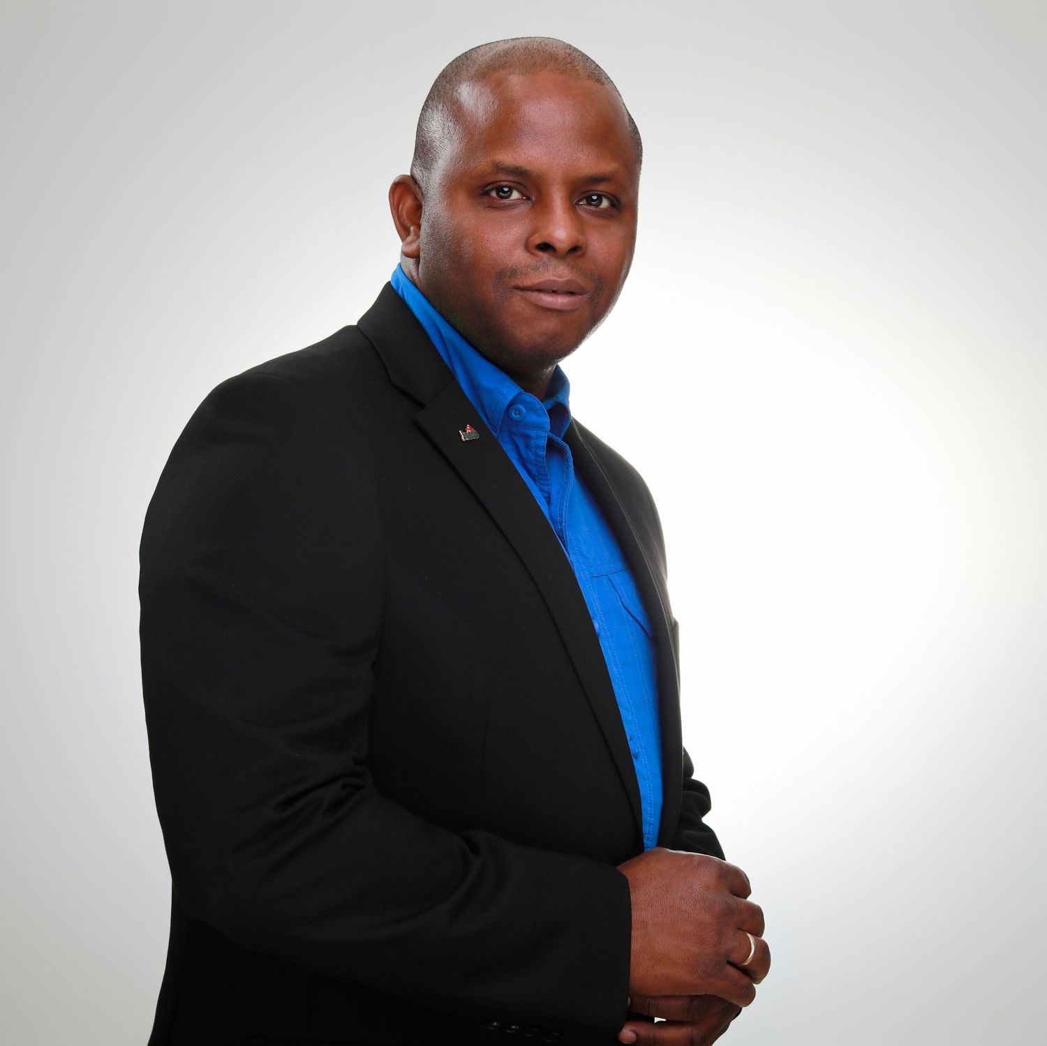 Business professional in black blazer and blue shirt poses against grey background.