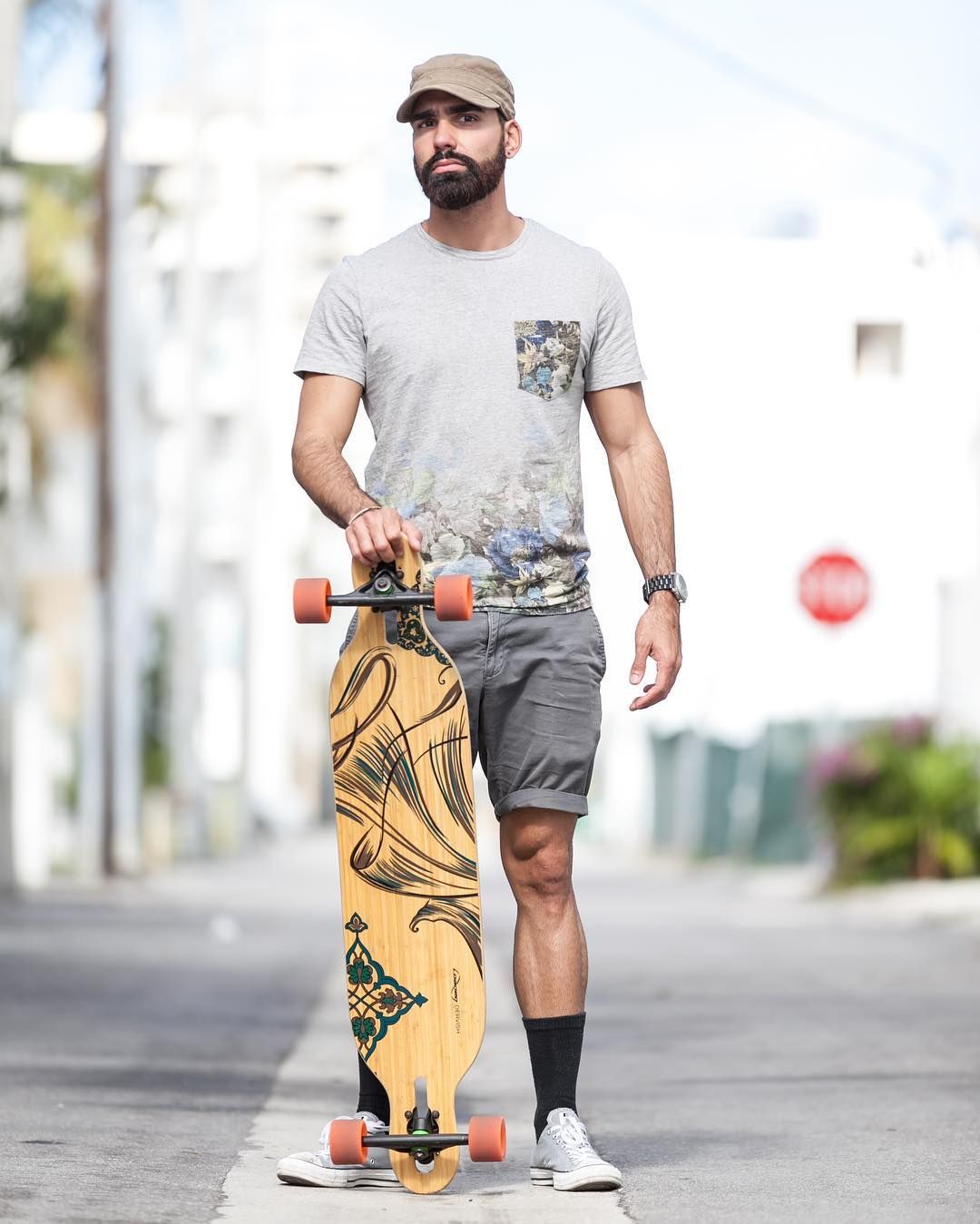 Person in casual wear holding a longboard with artistic design on an urban street.