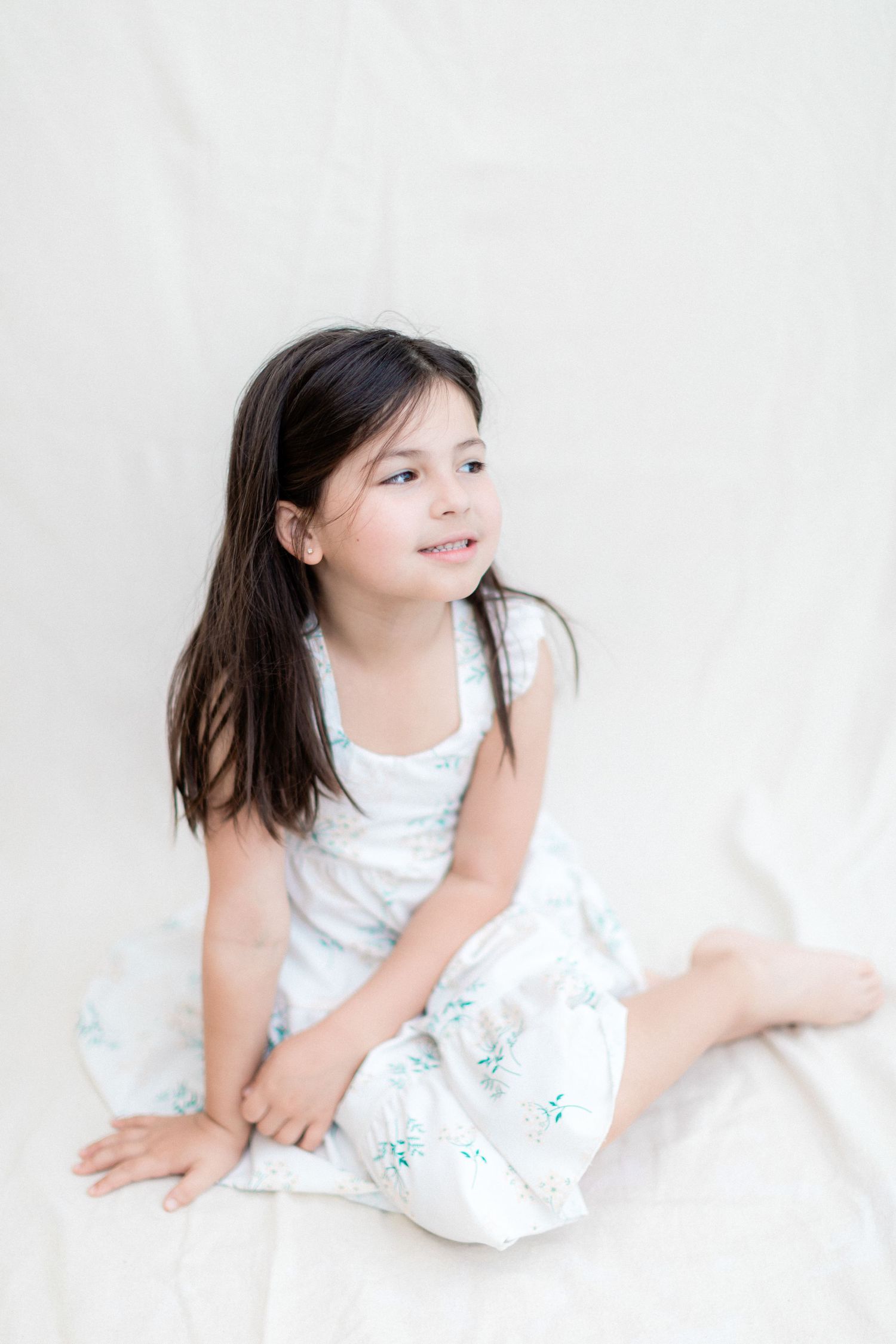 A young person in a white floral dress sitting against a light background.