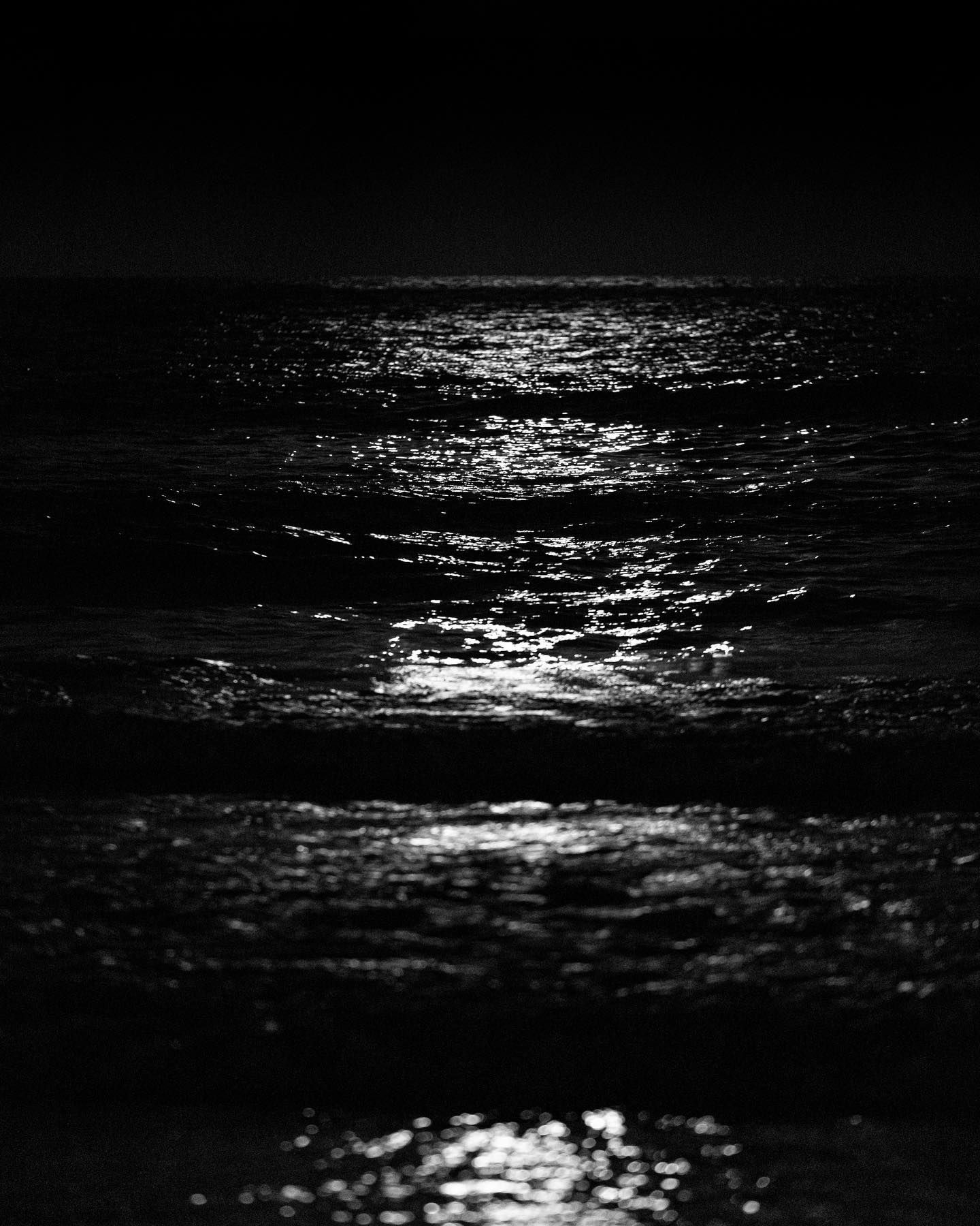 Moonlight reflecting on dark ocean waves in black and white.