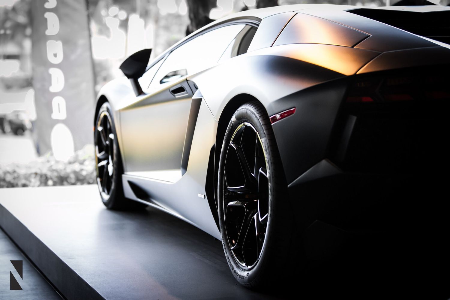 Close-up shot of a sleek black Lamborghini sports car with custom black wheels against blurred background.